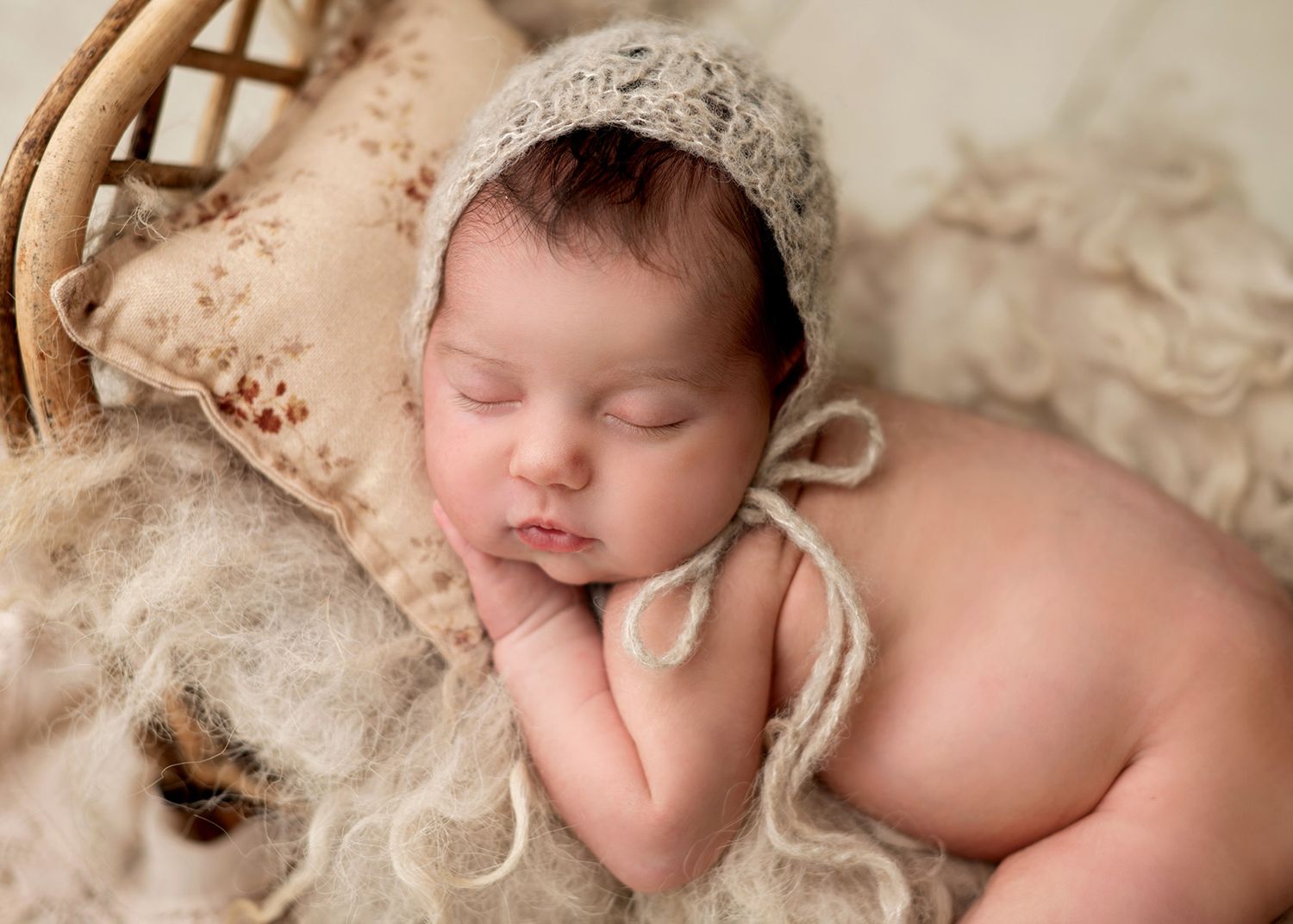 A sleeping newborn baby wrapped in soft beige textiles rests peacefully during a professional photo session, Victoria BC