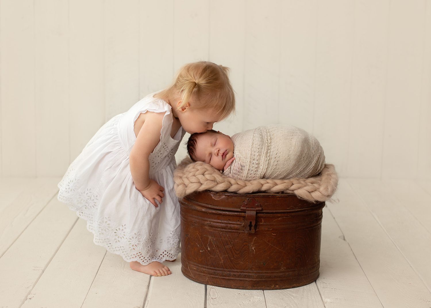 Toddler kissing a newborn resting on a vintage  decorative prop, Victoria BC newborn studio photography