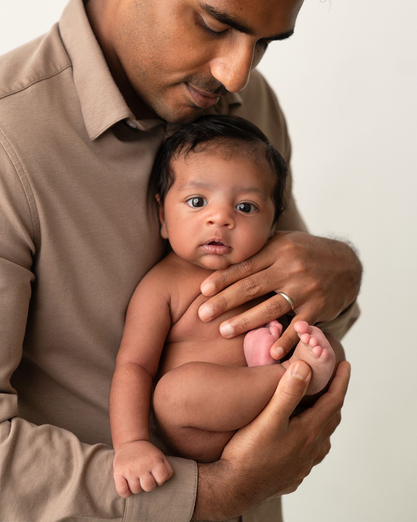 father holding newborn baby as baby looks towards camera, soft studio lighting, Victoria newborn photography