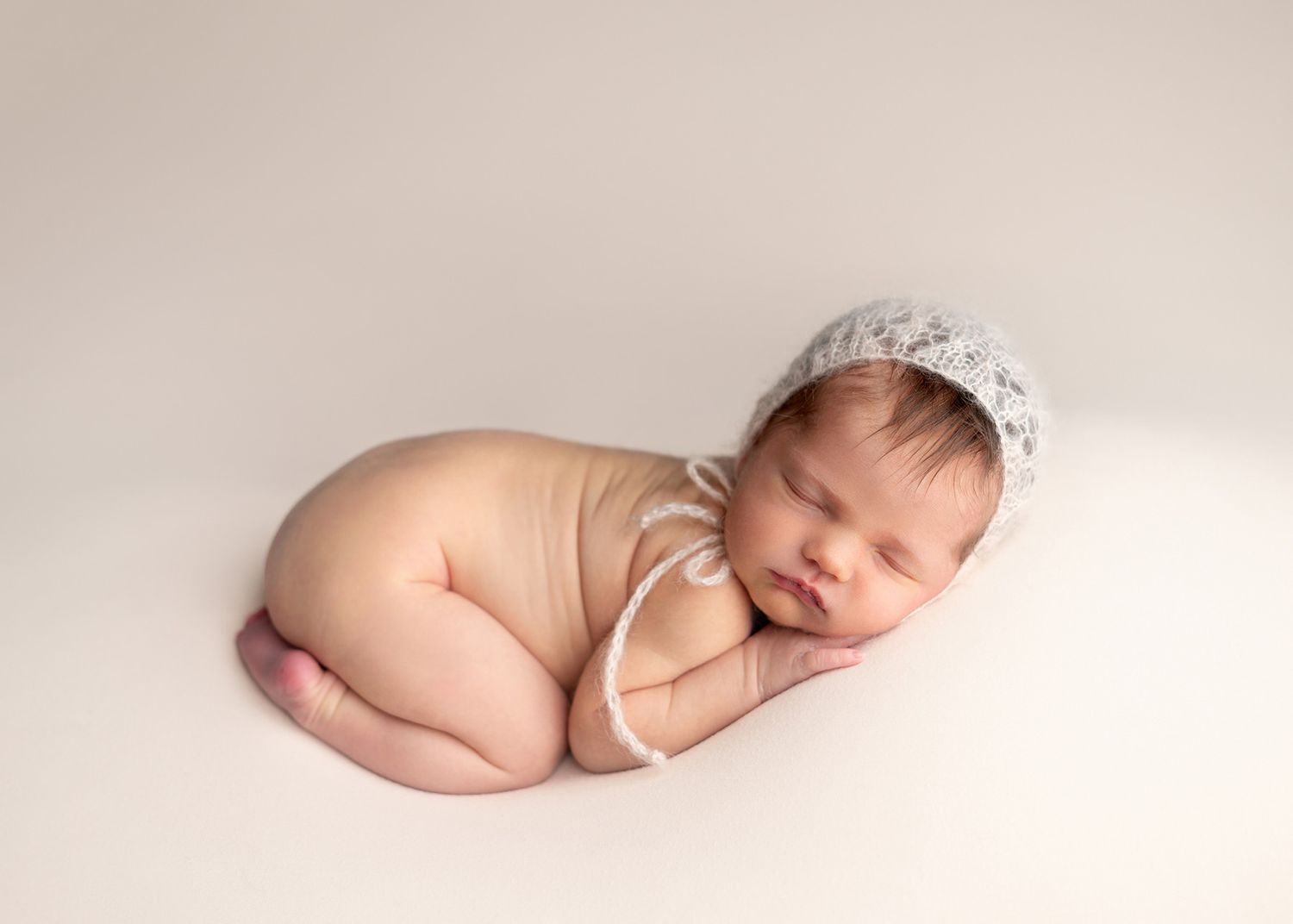 Peaceful sleeping newborn baby wearing delicate lace bonnet posed on cream backdrop in studio setting, Victoria BC photography