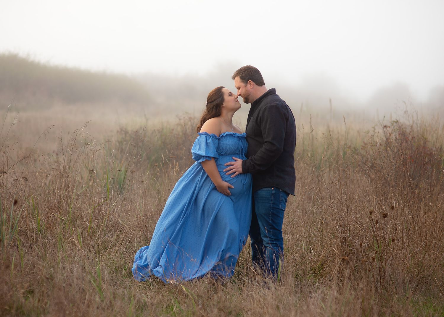 An expecting couple in a misty field embraces romantically at sunset, Victoria BC outdoor maternity session