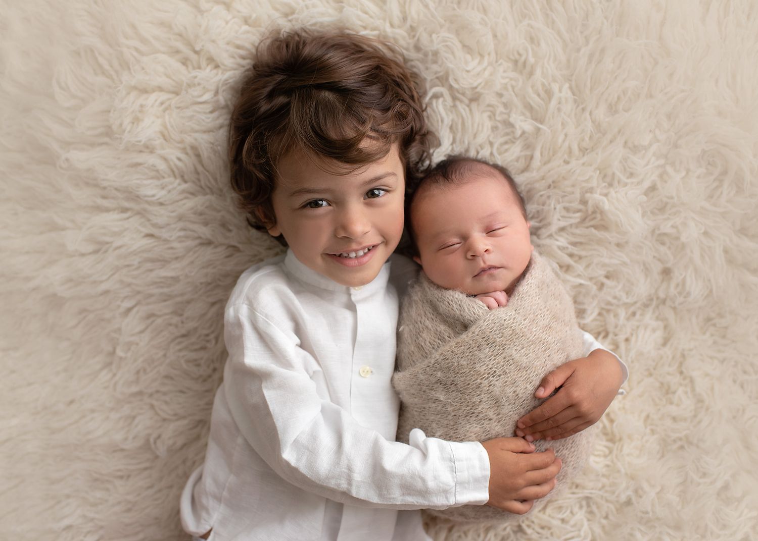 older sibling lying on soft cream carpet gently holding newborn baby, soft studio lighting, Victoria BC newborn photography
