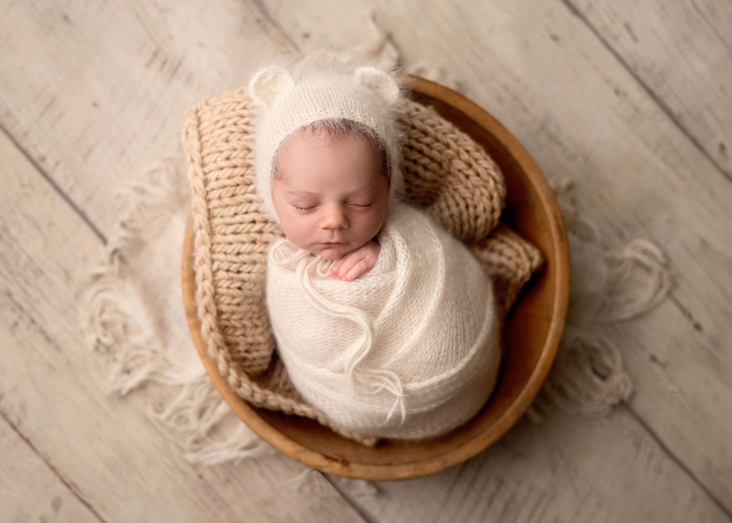 Newborn baby wrapped in white blanket lying in wooden bowl on rustic wooden floor, Victoria BC newborn photography