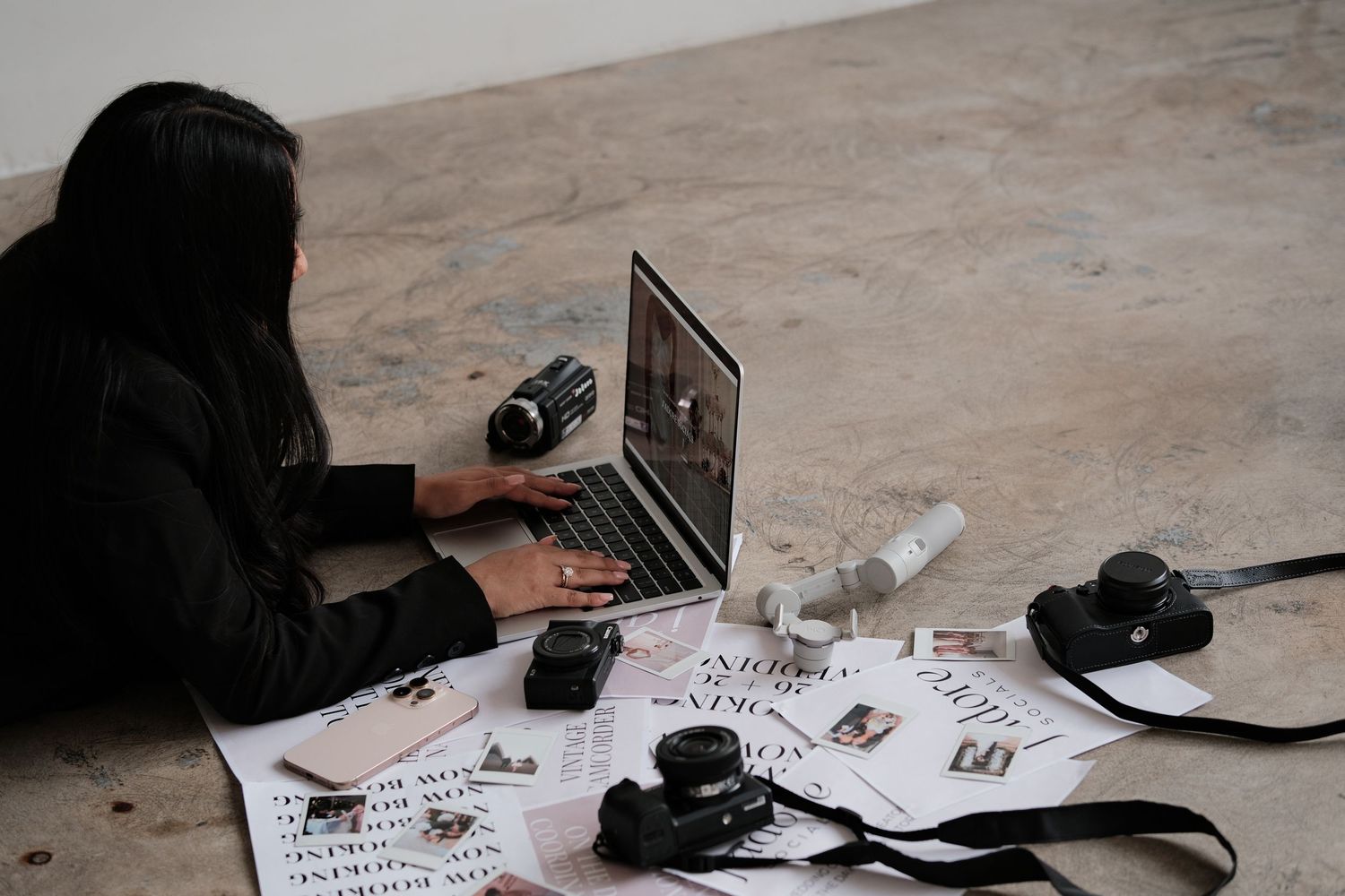 Flatlay of workspace with laptop, camera equipment and scattered papers.