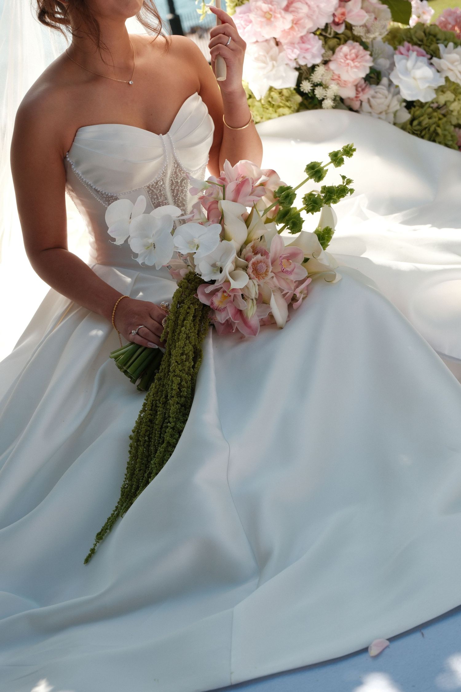 Bride in strapless white ball gown holding elegant bouquet of pink orchids and white flowers at wedding ceremony.