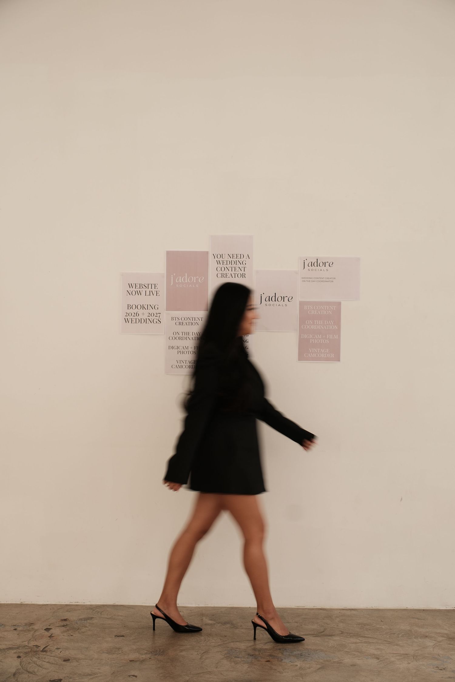 Silhouette of person in black dress walking past wall with text.