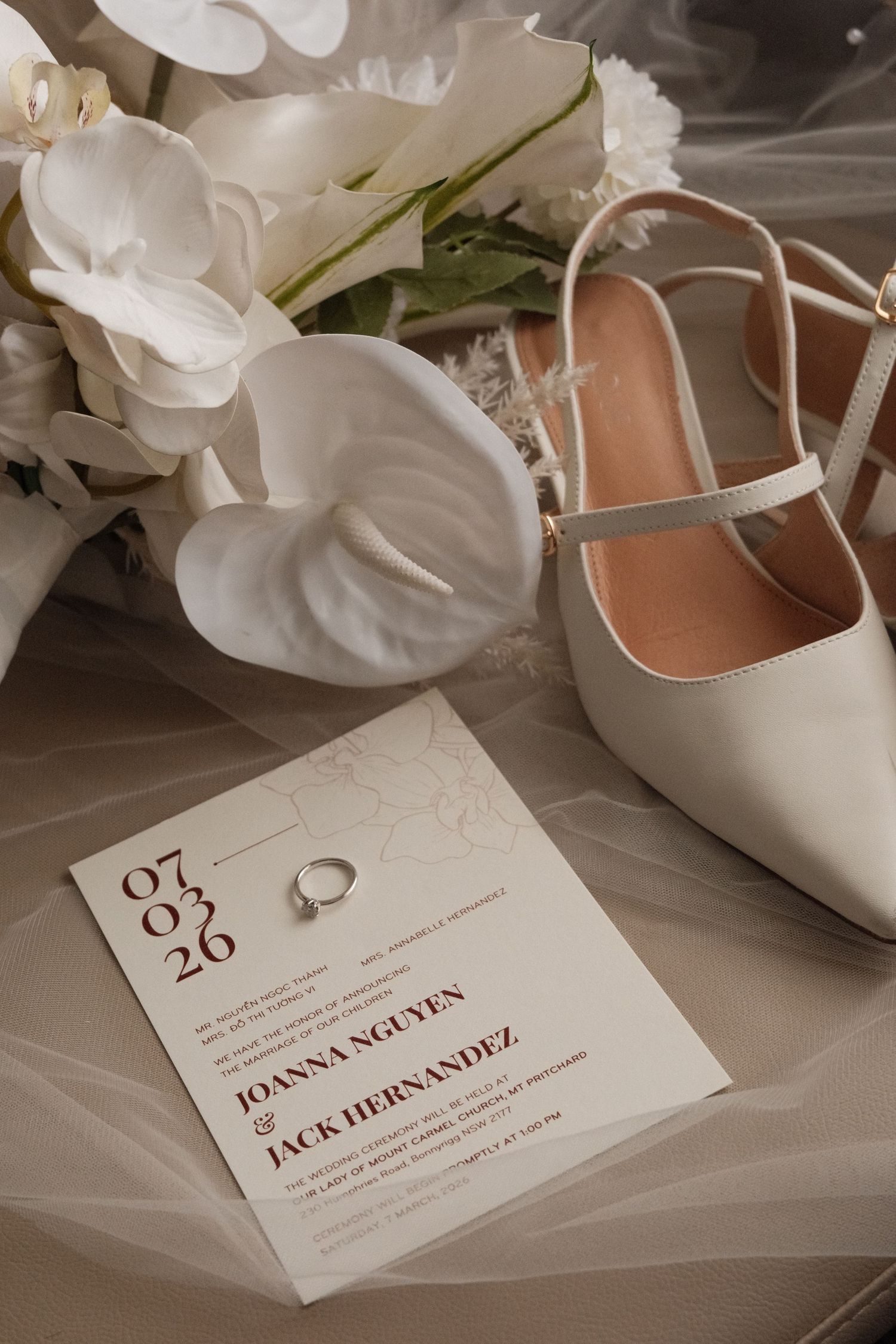 Elegant white wedding place cards and shoes arranged with soft white floral decorations on a neutral surface.