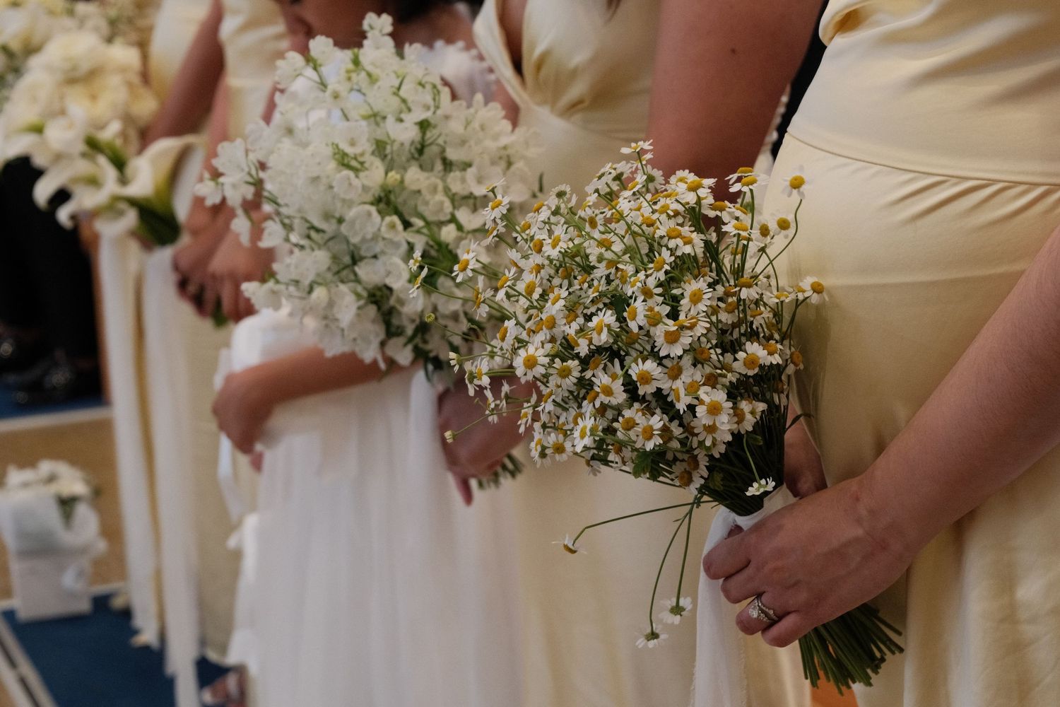 Bridesmaids in yellow dresses holding white daisy bouquets at a wedding ceremony.