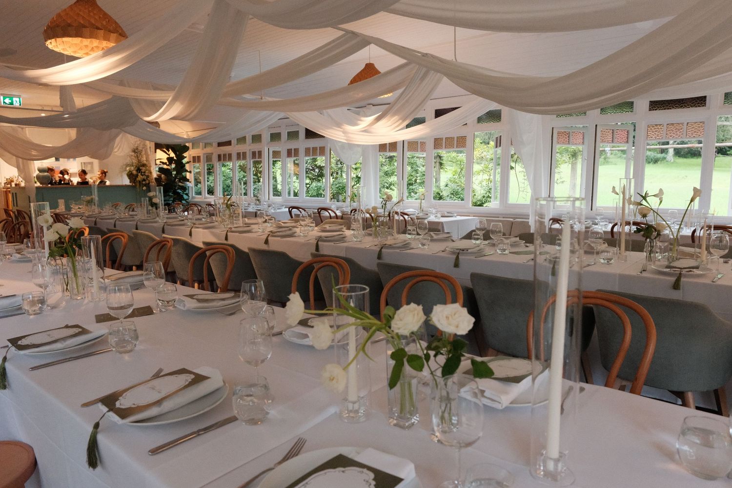 Elegant wedding reception setup under draped white fabric ceiling with copper pendant lights and white table settings.