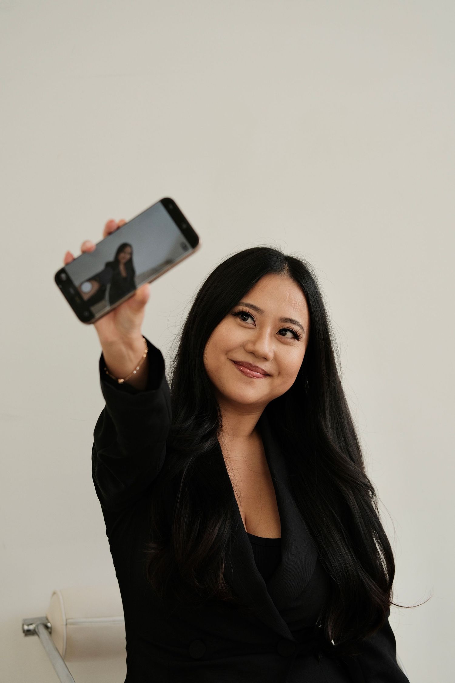 Person in black outfit posing with a mobile phone against neutral background.