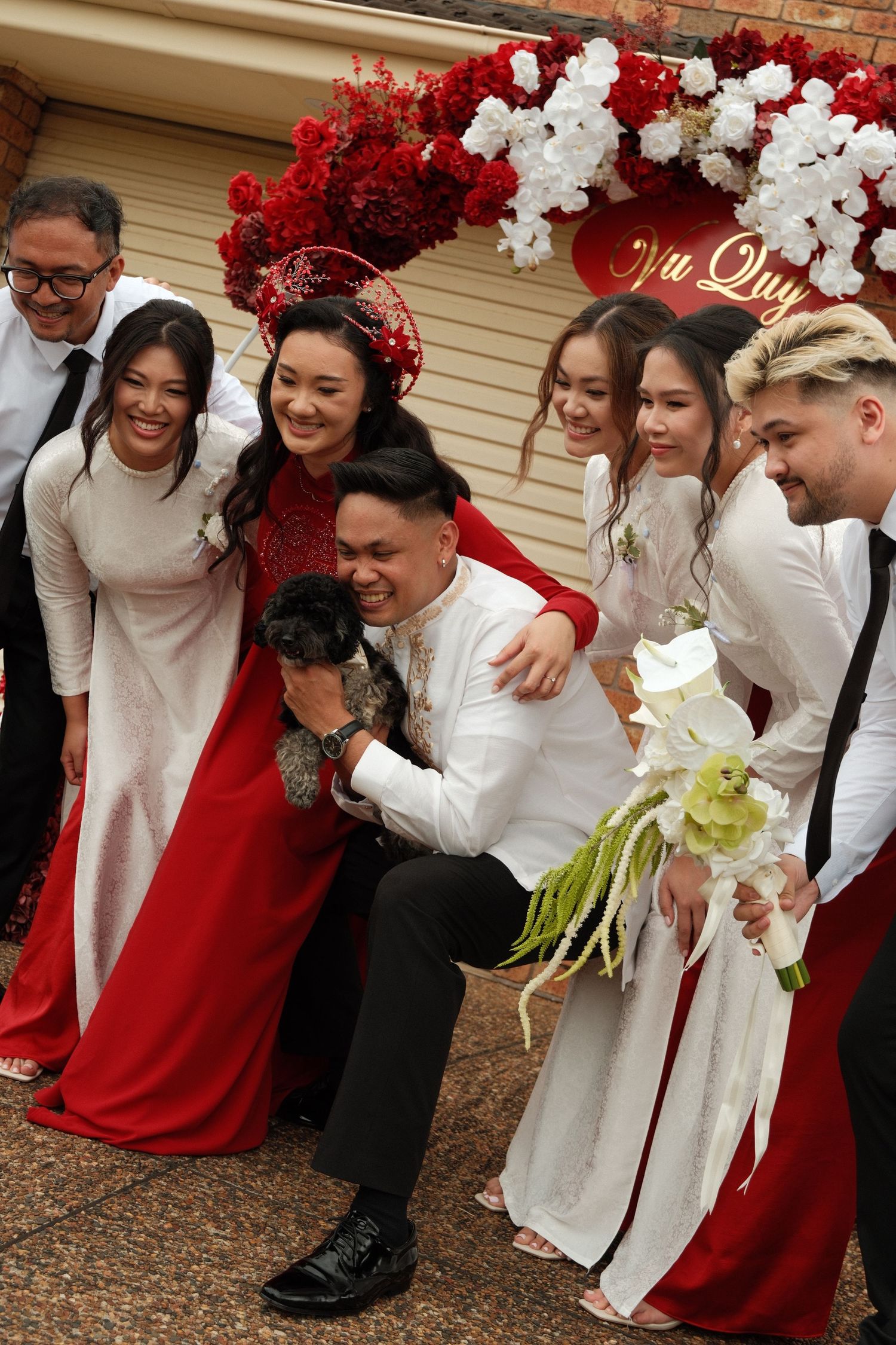 A group wearing red and white outfits poses together with floral decorations in the background.