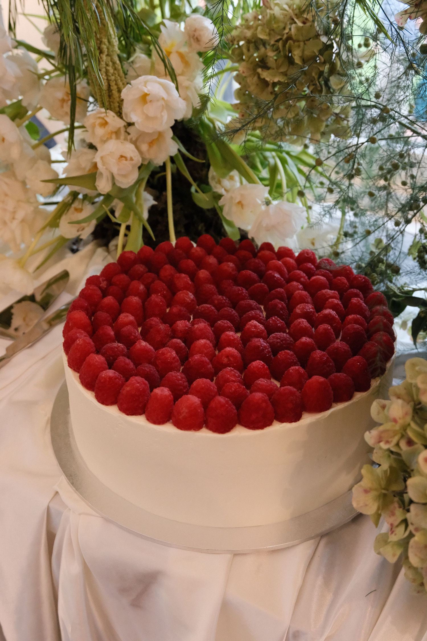 A white bowl filled with fresh red raspberries surrounded by delicate white floral arrangements.