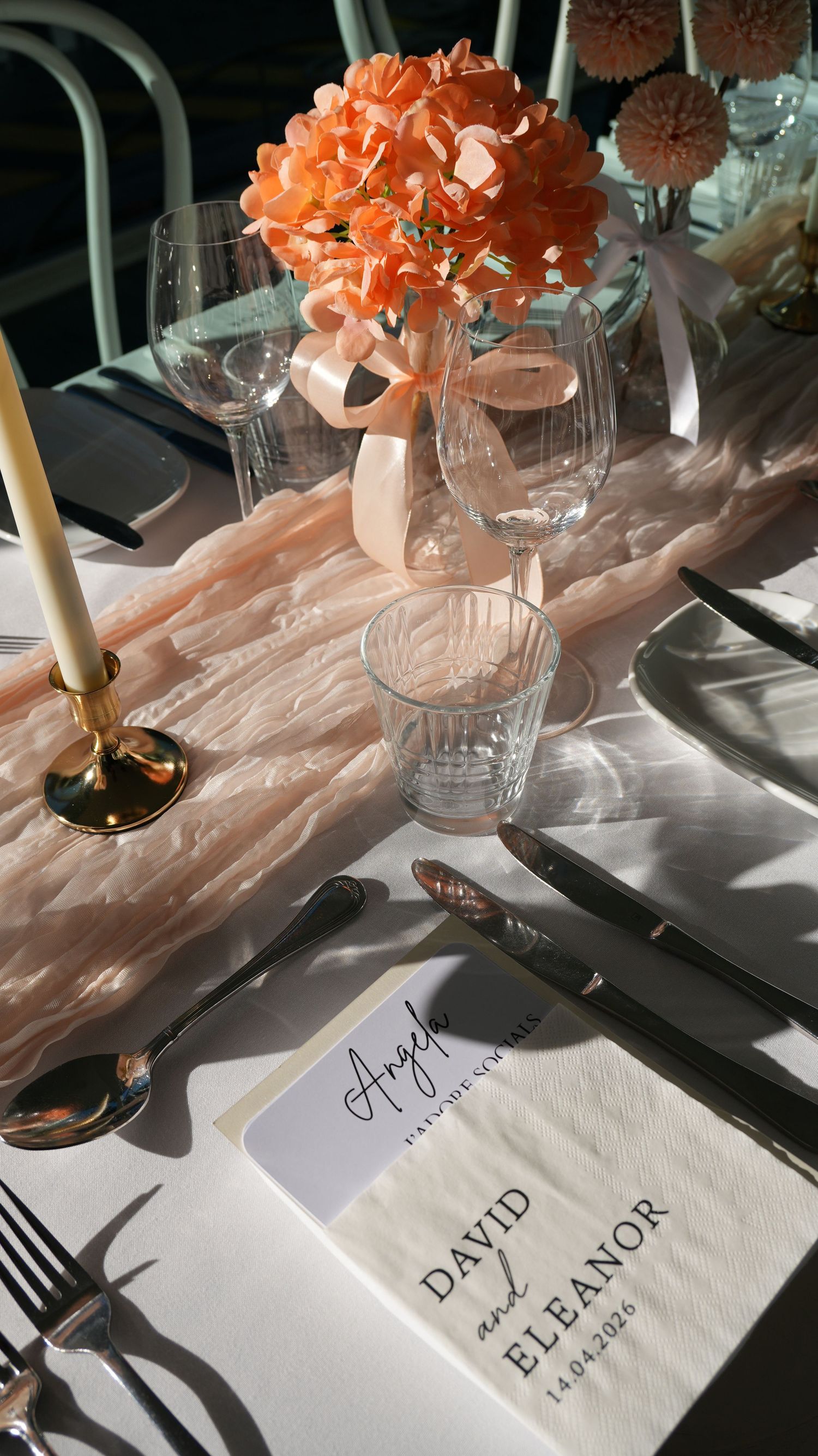 Elegant wedding table setting with peach floral centerpiece, gold candlesticks, crystal glasses, and personalized David and Eleanor napkins.