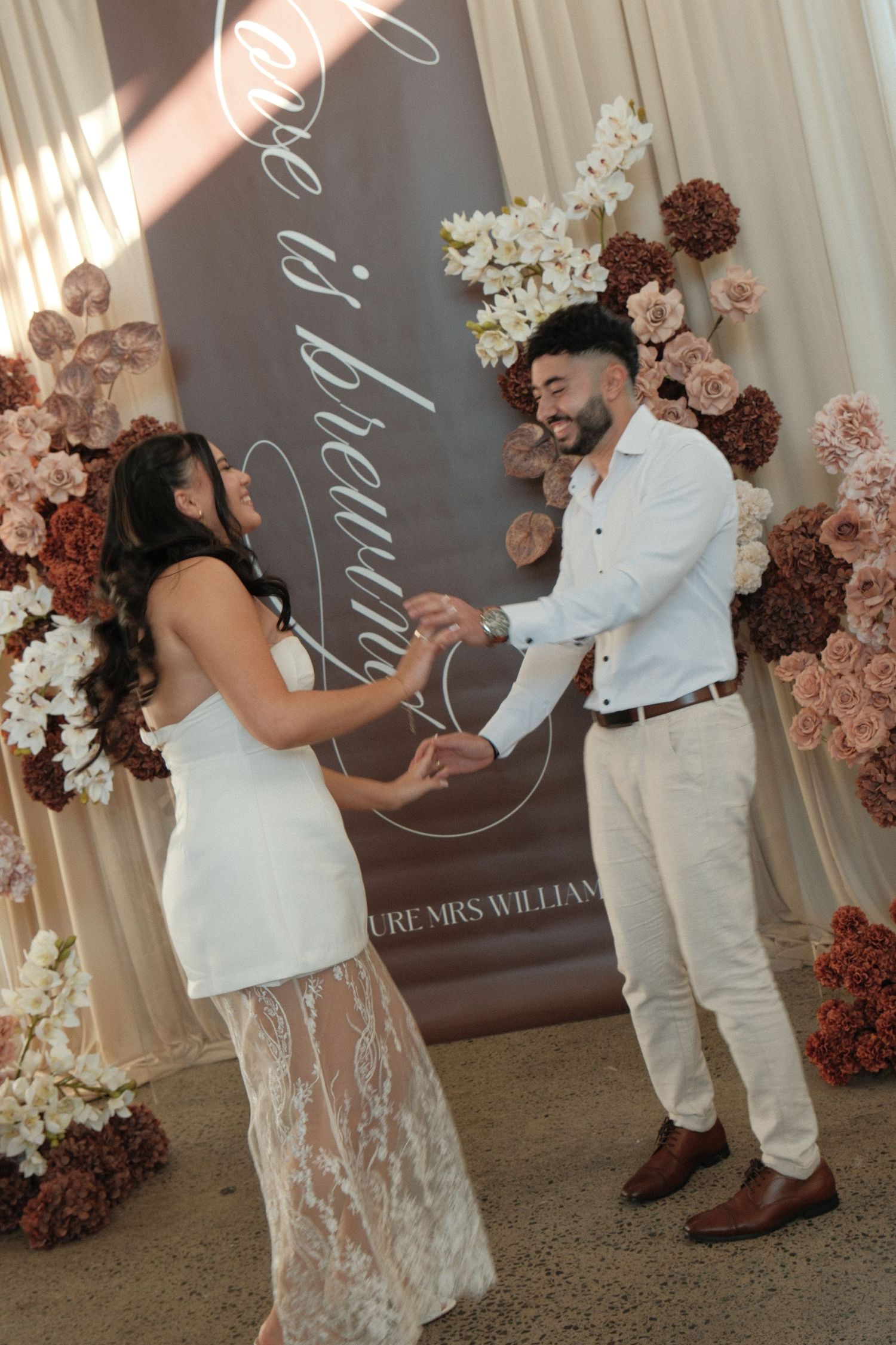 Couple exchanging rings at elegant wedding ceremony with floral arch backdrop featuring blush and burgundy flowers.