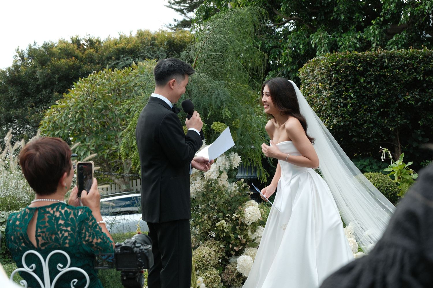 Wedding ceremony guests gather outdoors in a lush garden setting during a summer celebration.