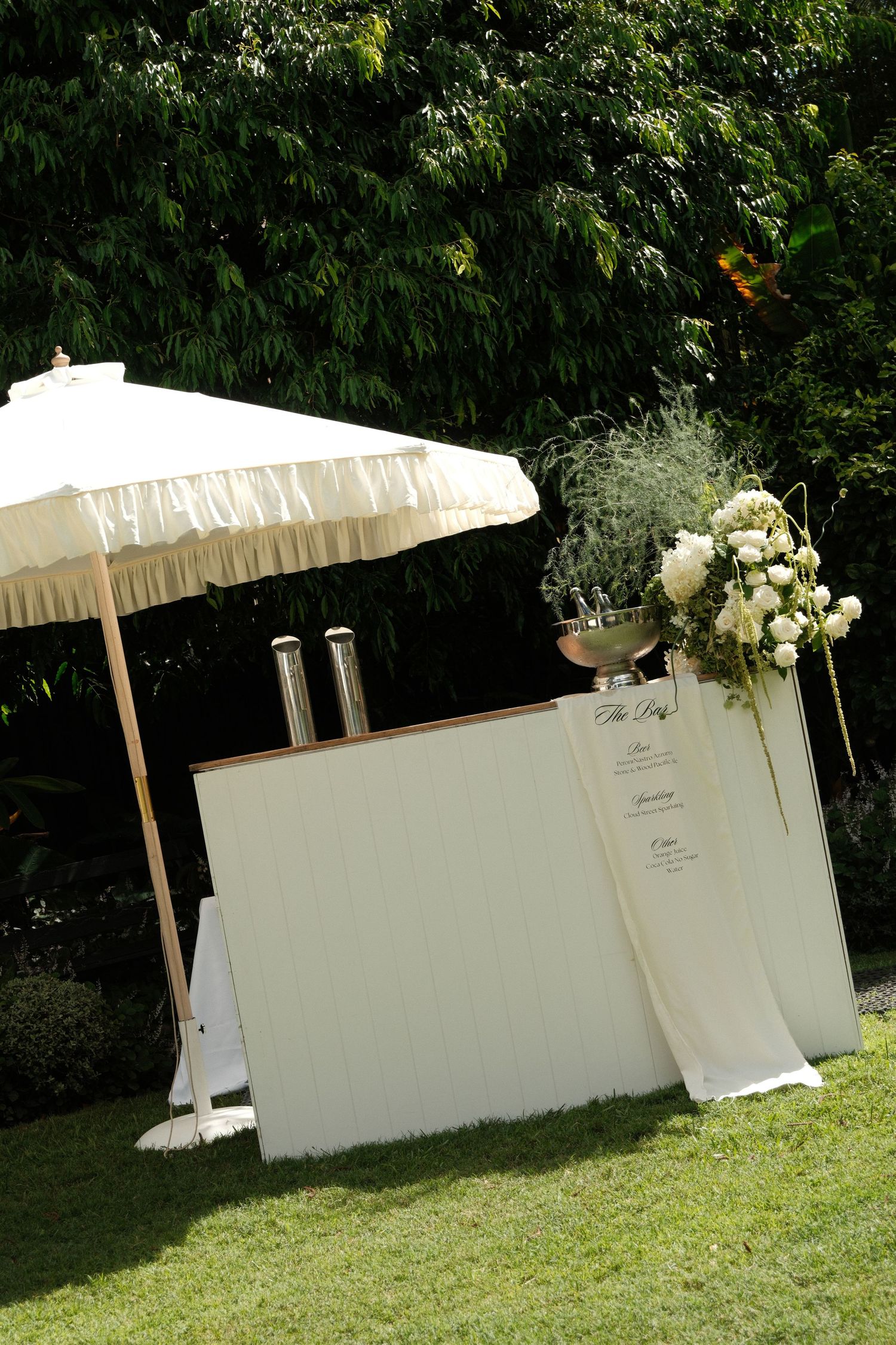 White decorative umbrellas and floral arrangements line an outdoor wedding venue wall.