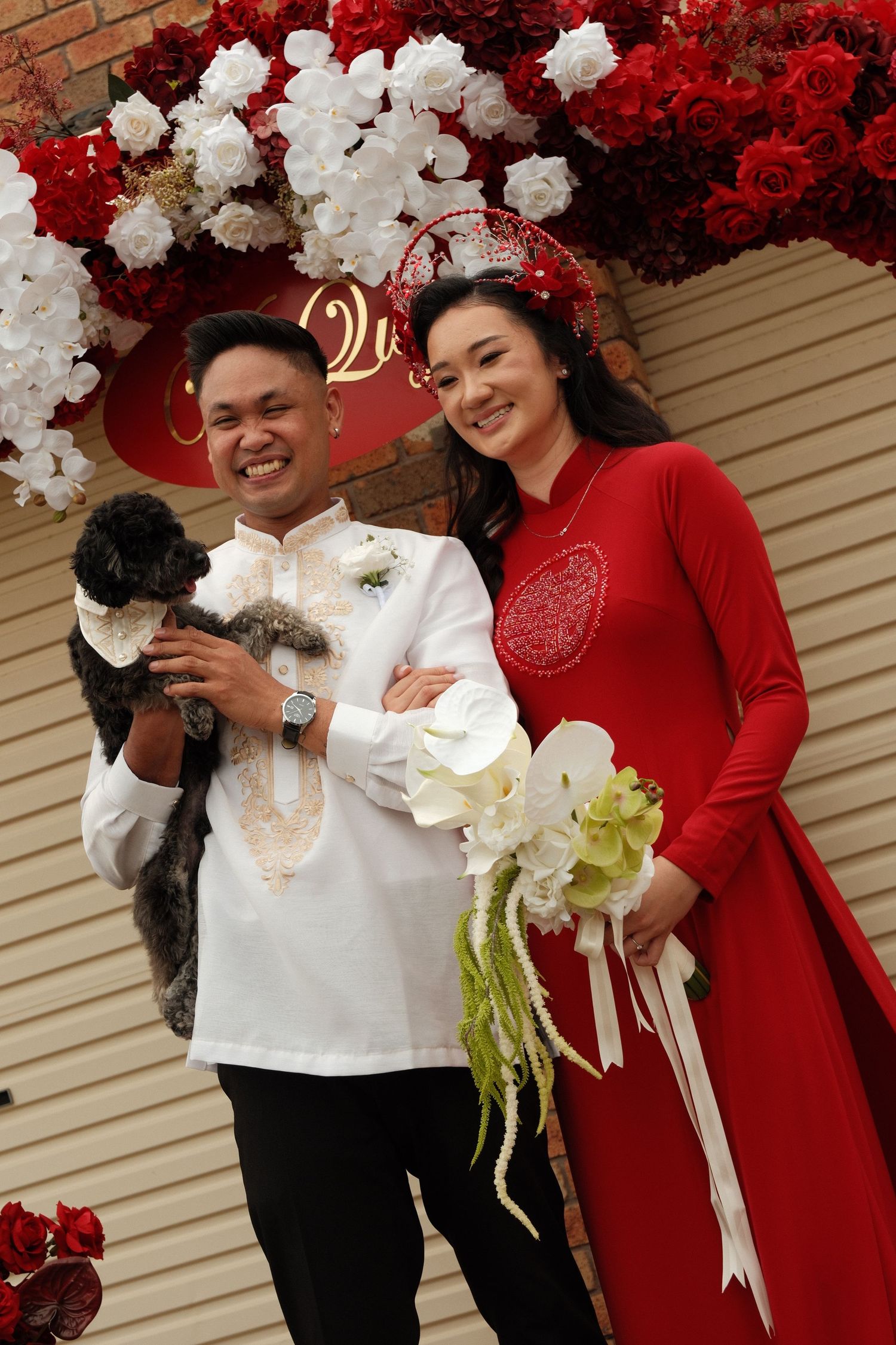 A wedding couple shares joyful moments in front of a red and white floral backdrop.