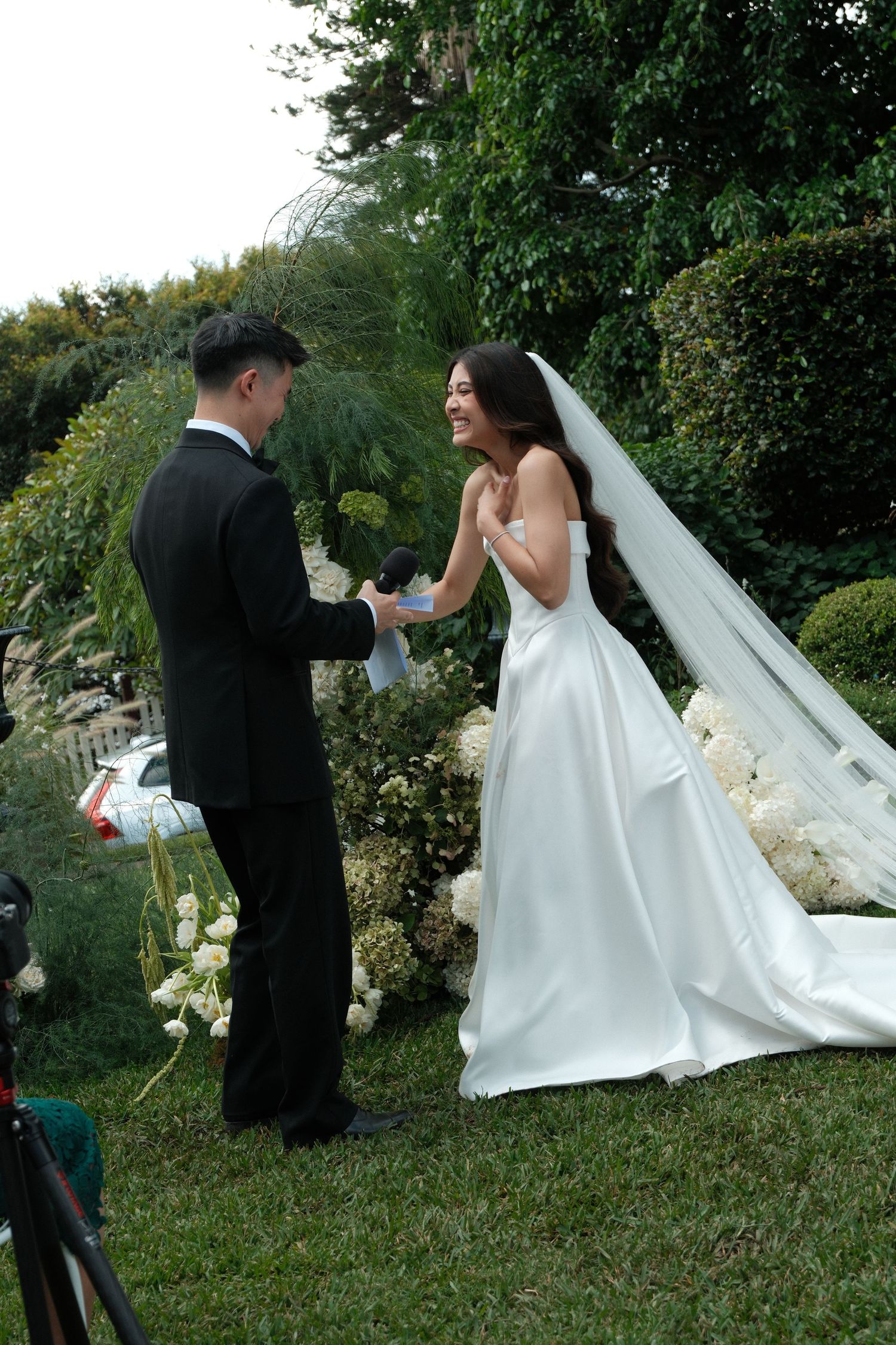 A couple exchanges vows during an outdoor garden wedding ceremony with lush greenery and white floral decorations.
