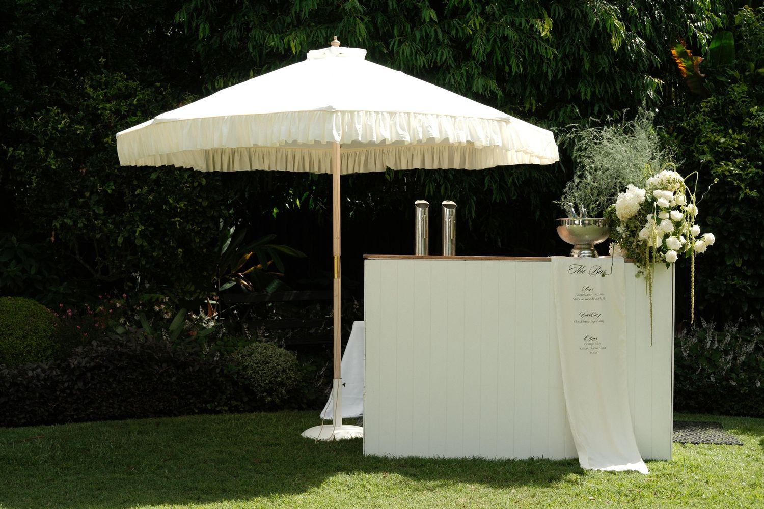 White tent umbrellas and seating arrangements set up for an outdoor event in a lush garden setting.