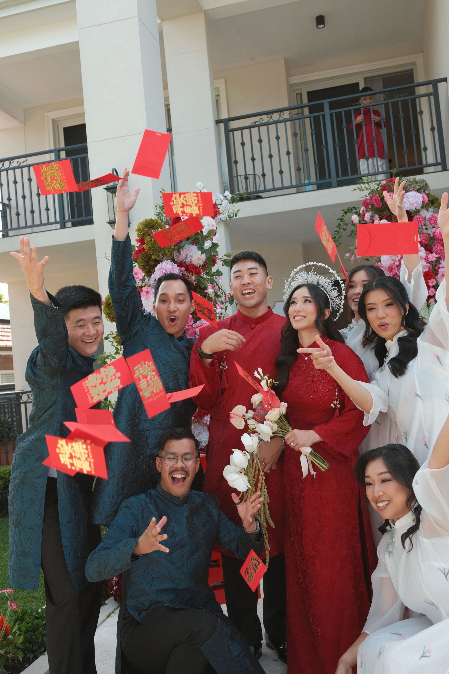 A group wearing red and white outfits celebrates joyfully while holding red envelopes and flowers during festivities.