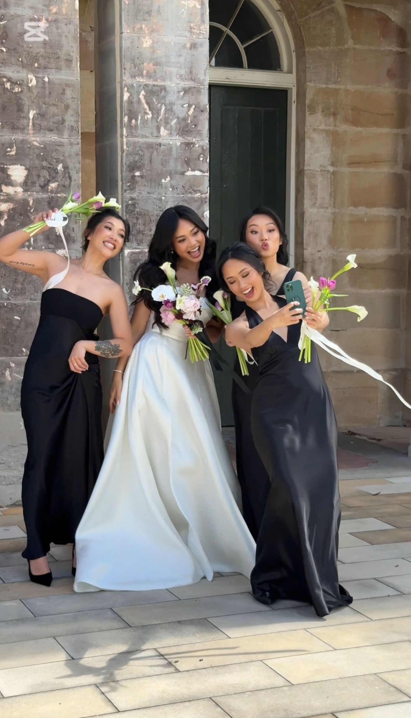 Wedding party striking fun poses against stone building exterior.