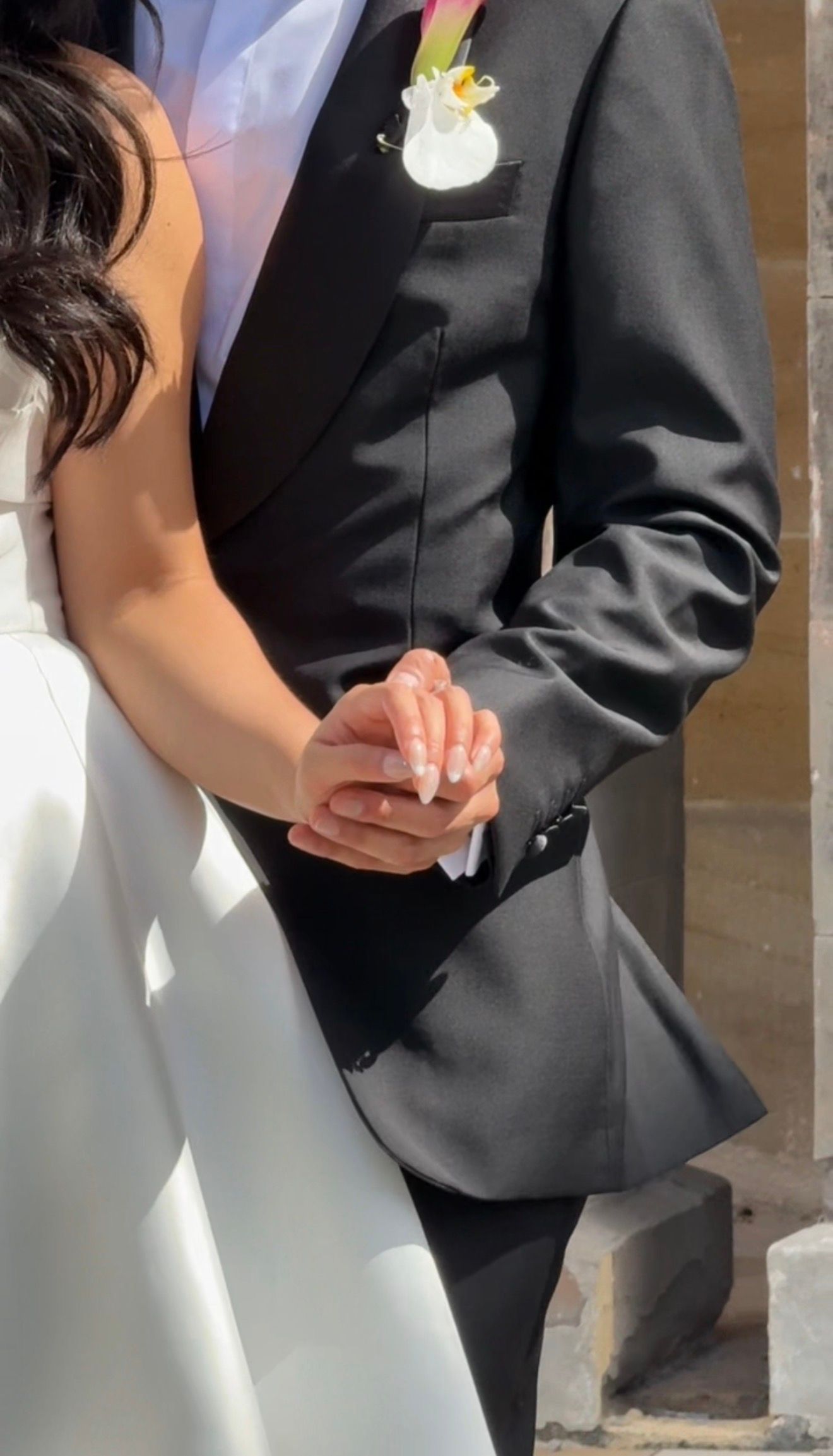 Close-up details of formal wedding attire showing black suit jacket and white dress fabric in sunlight.