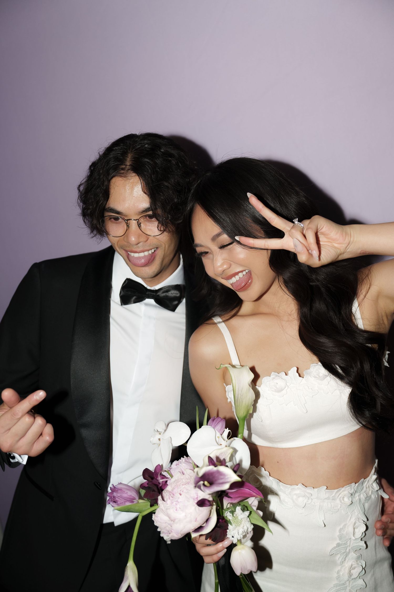 Playful wedding couple portraits in formal attire against purple backdrop with floral bouquet.