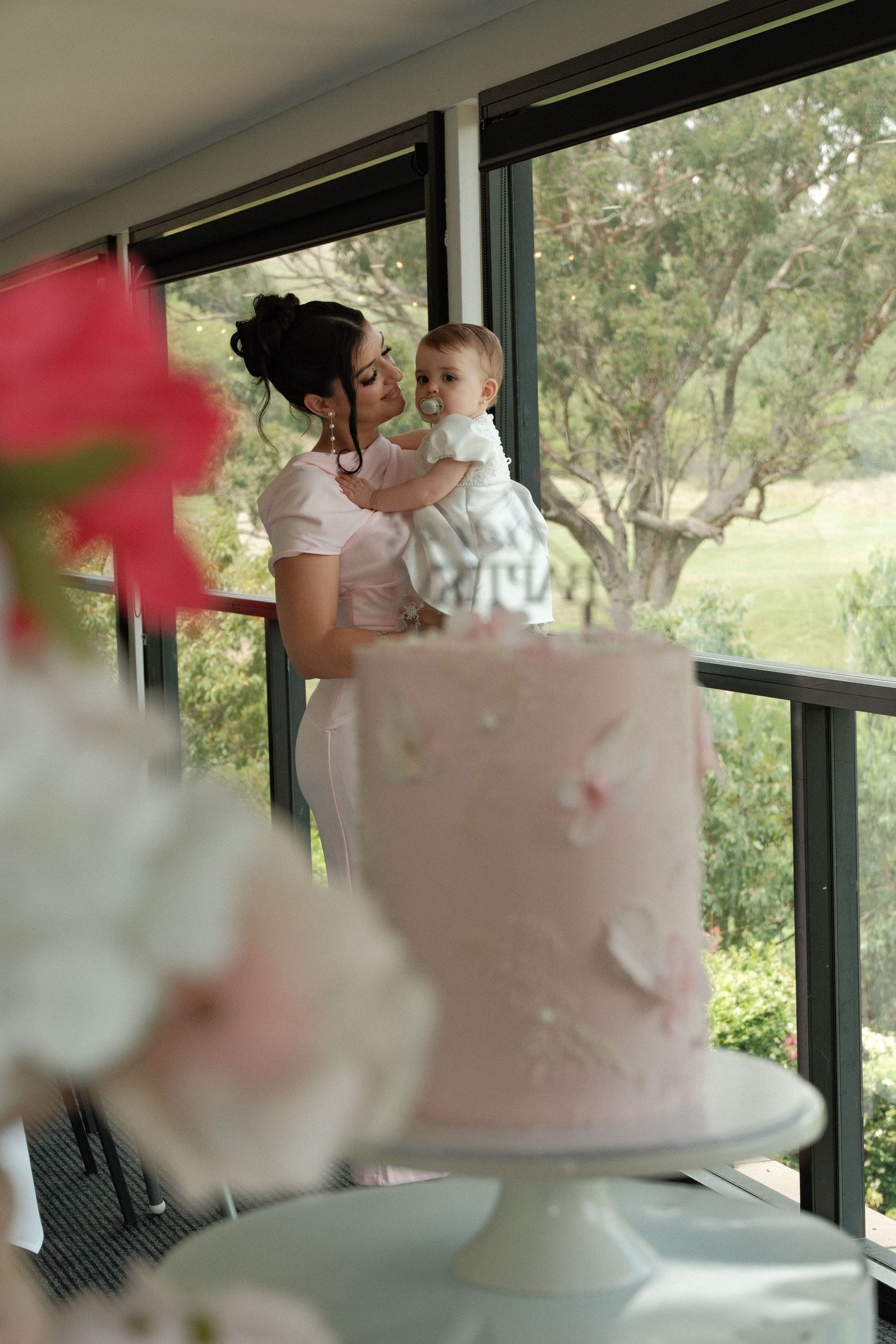 Pink wedding cake with cotton candy clouds displayed near windows in natural lighting.