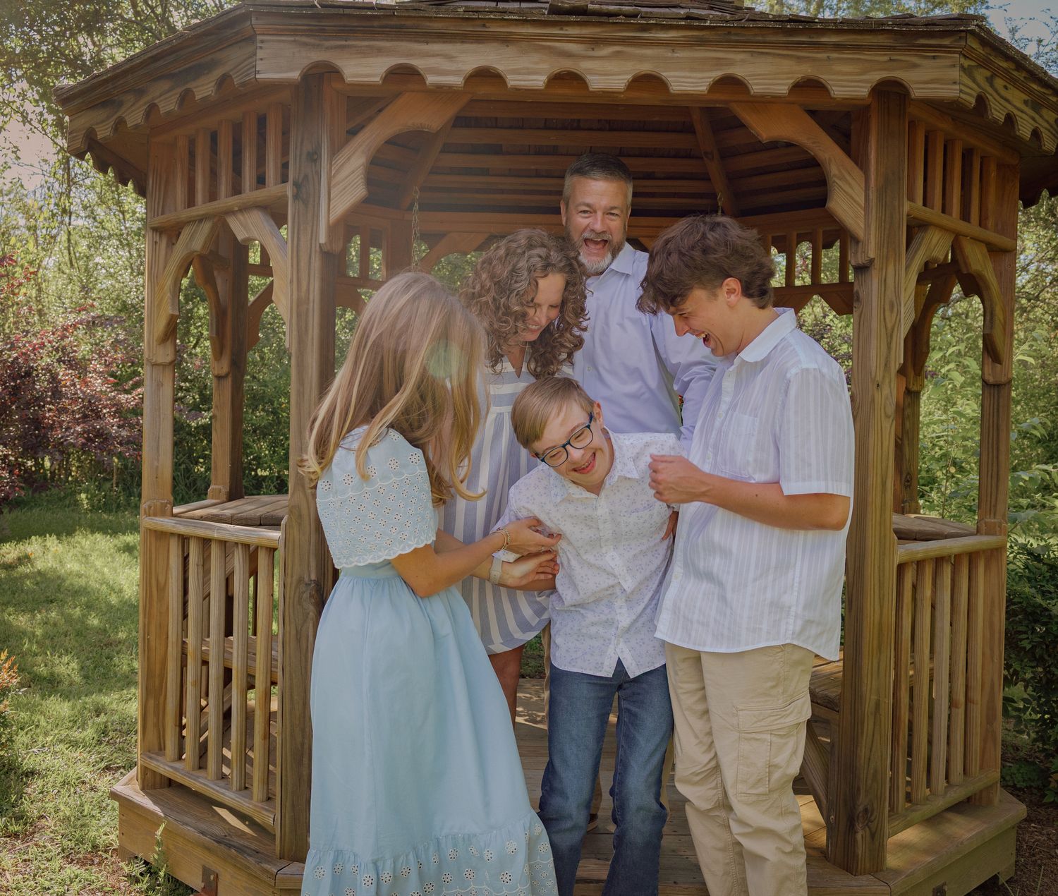 Friends share laughs and hugs inside a wooden gazebo on a sunny day.