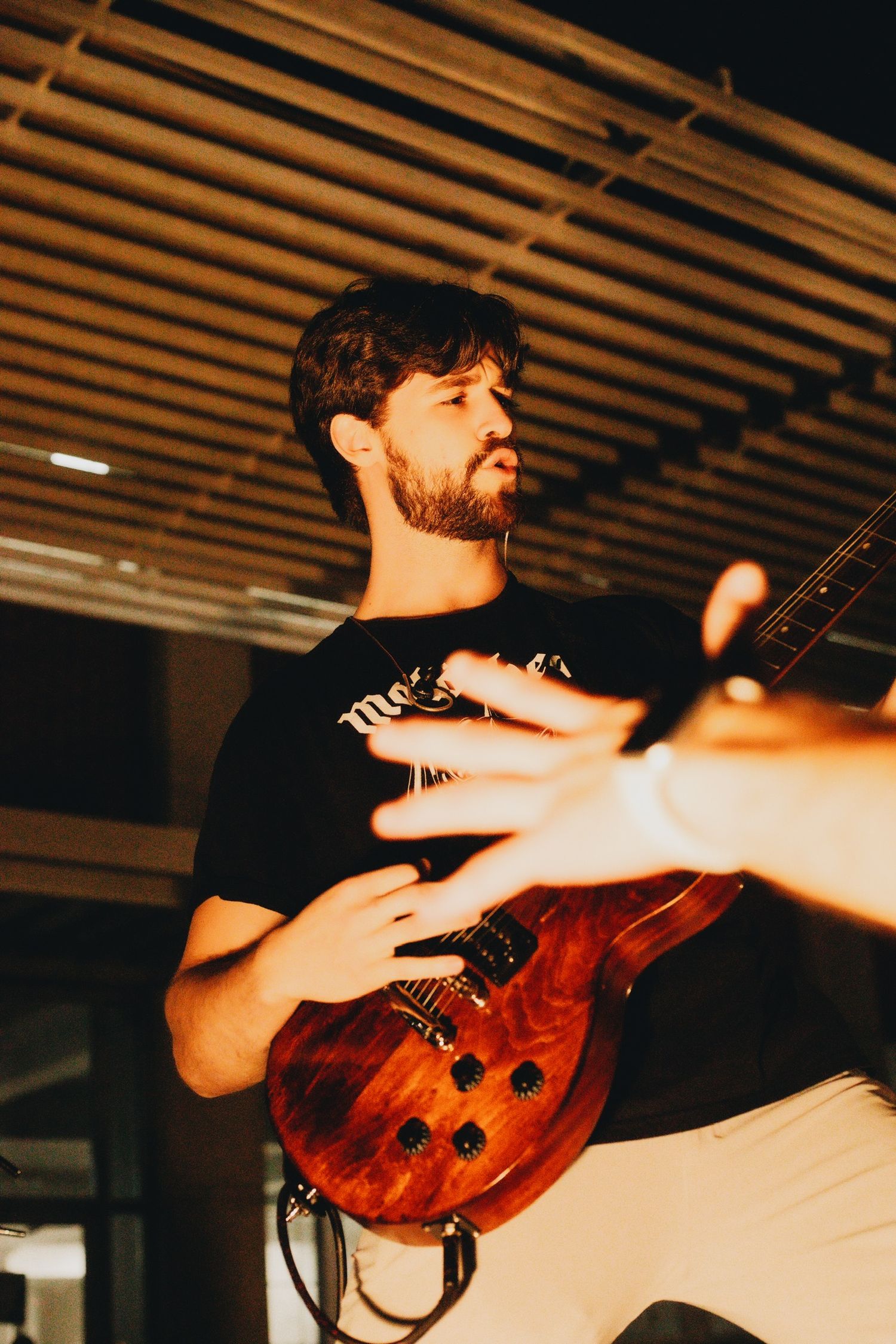Guitarist playing a wooden electric guitar under warm lighting.