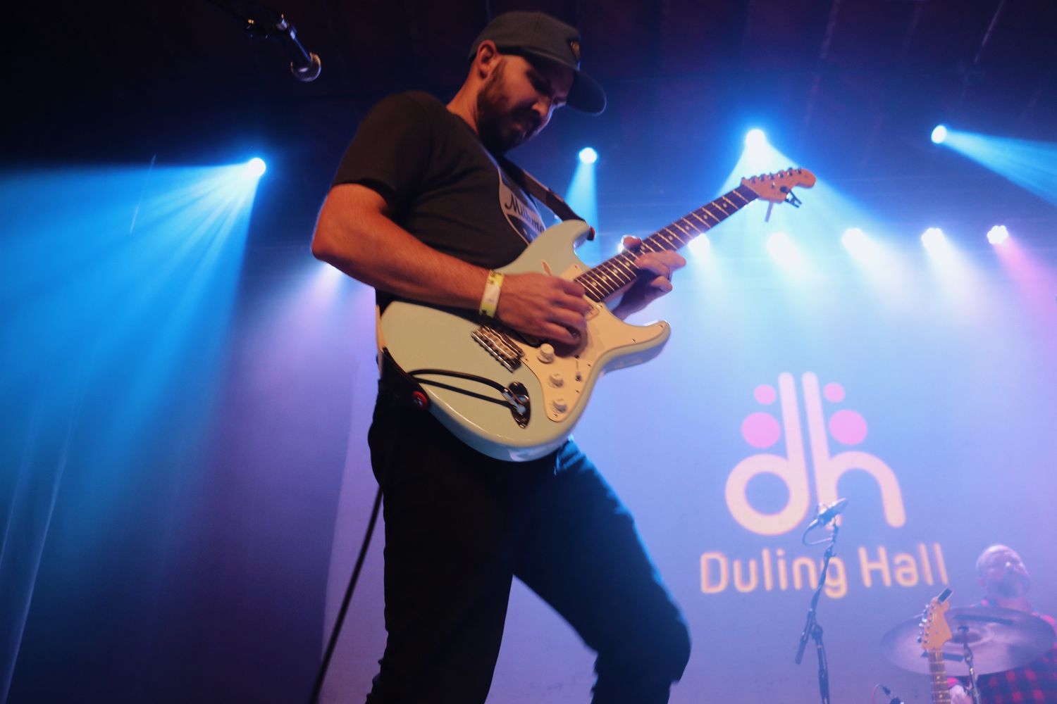 Concert performance at Dulina Hall with dramatic blue stage lighting and silhouetted guitarist.