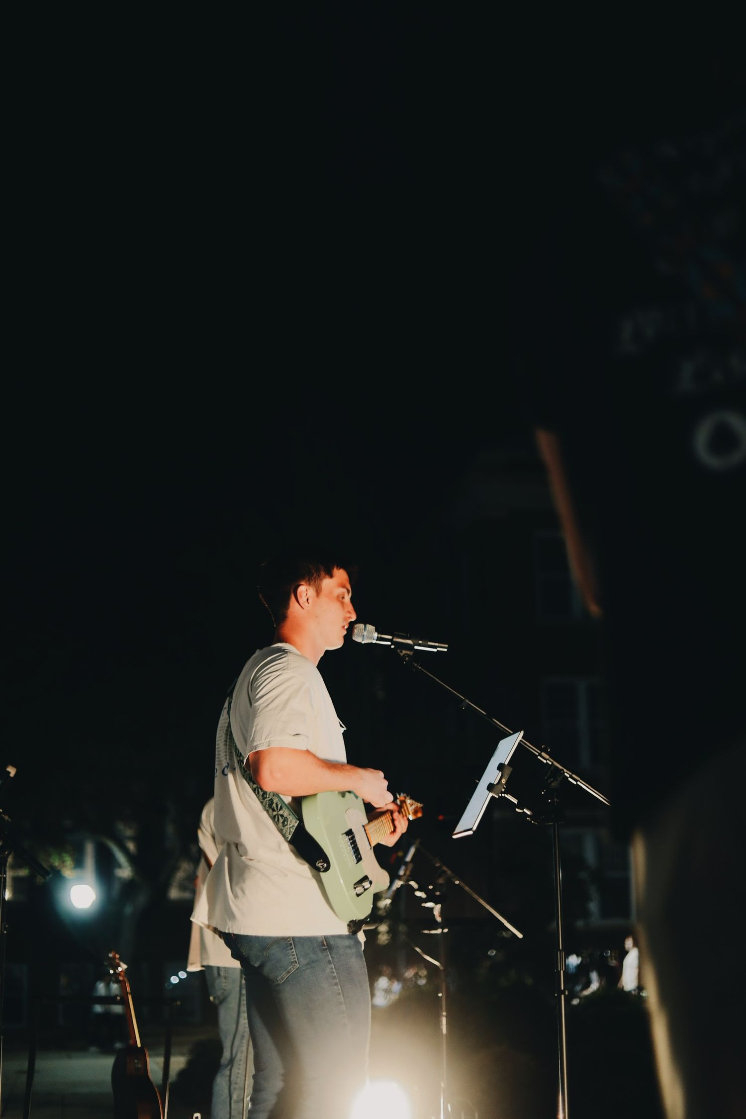 Musician singing into microphone while playing guitar during nighttime performance.