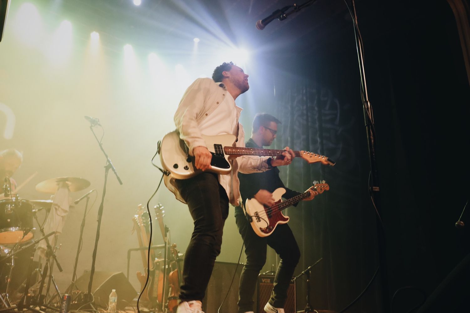 Band members performing with guitars on stage with dramatic backlighting.