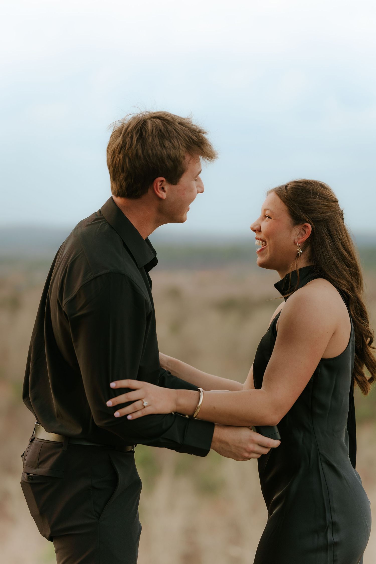Couple celebrating their engagement with genuine laughter and embraces outdoors.