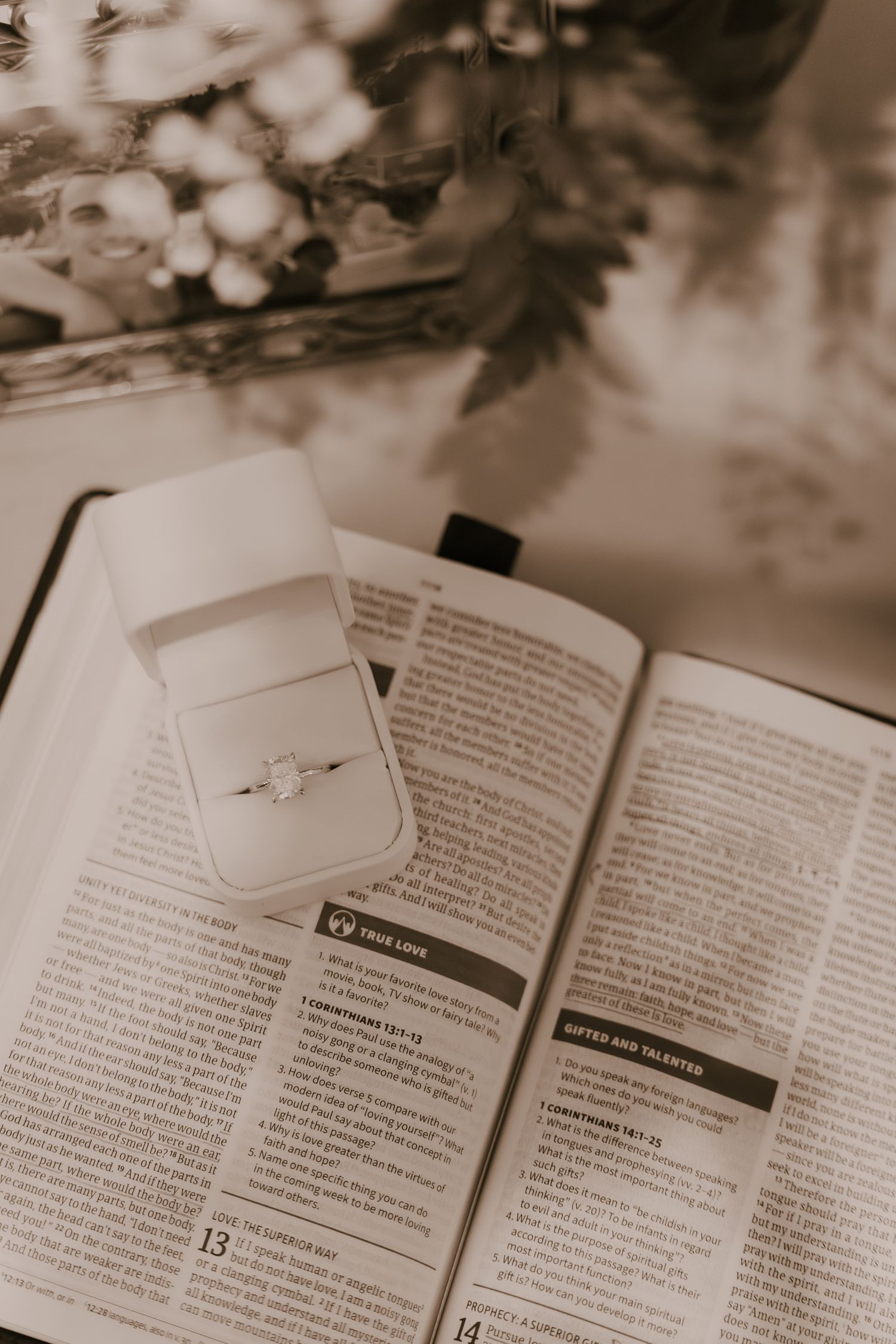 Open Bible with engagement ring placed between pages in soft focus.