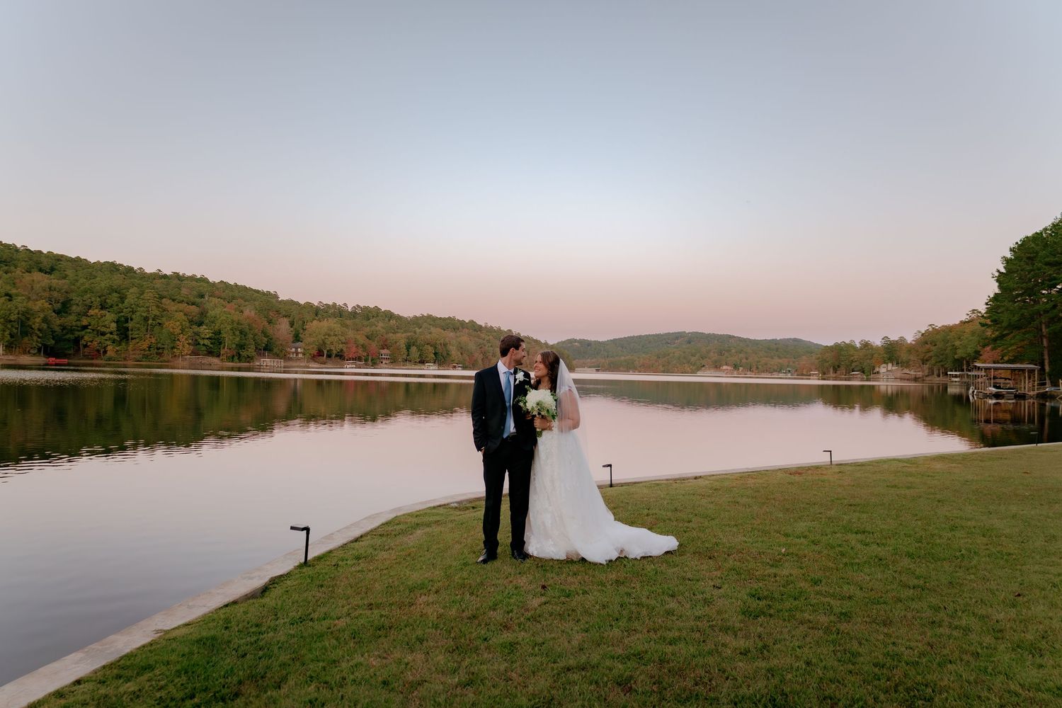 Wedding couple silhouetted against a serene lakeside view at dusk.