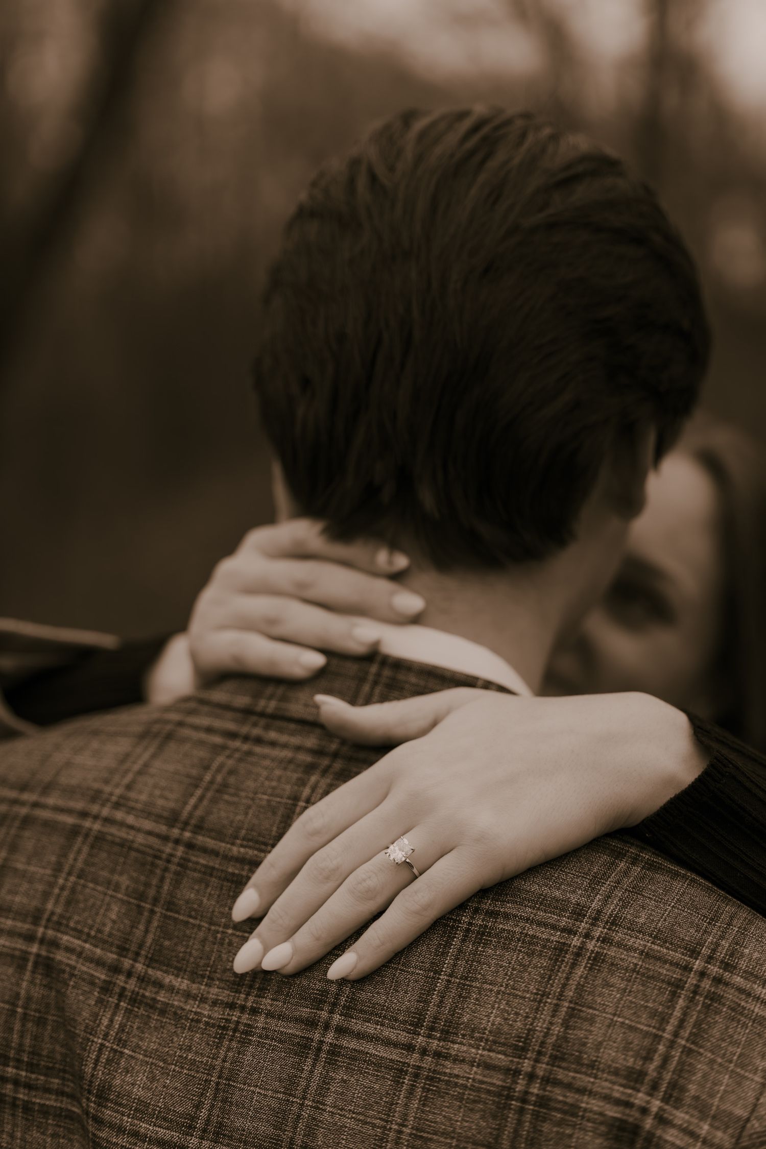 Close-up detail of a hand resting on a plaid-clothed shoulder in sepia tones.