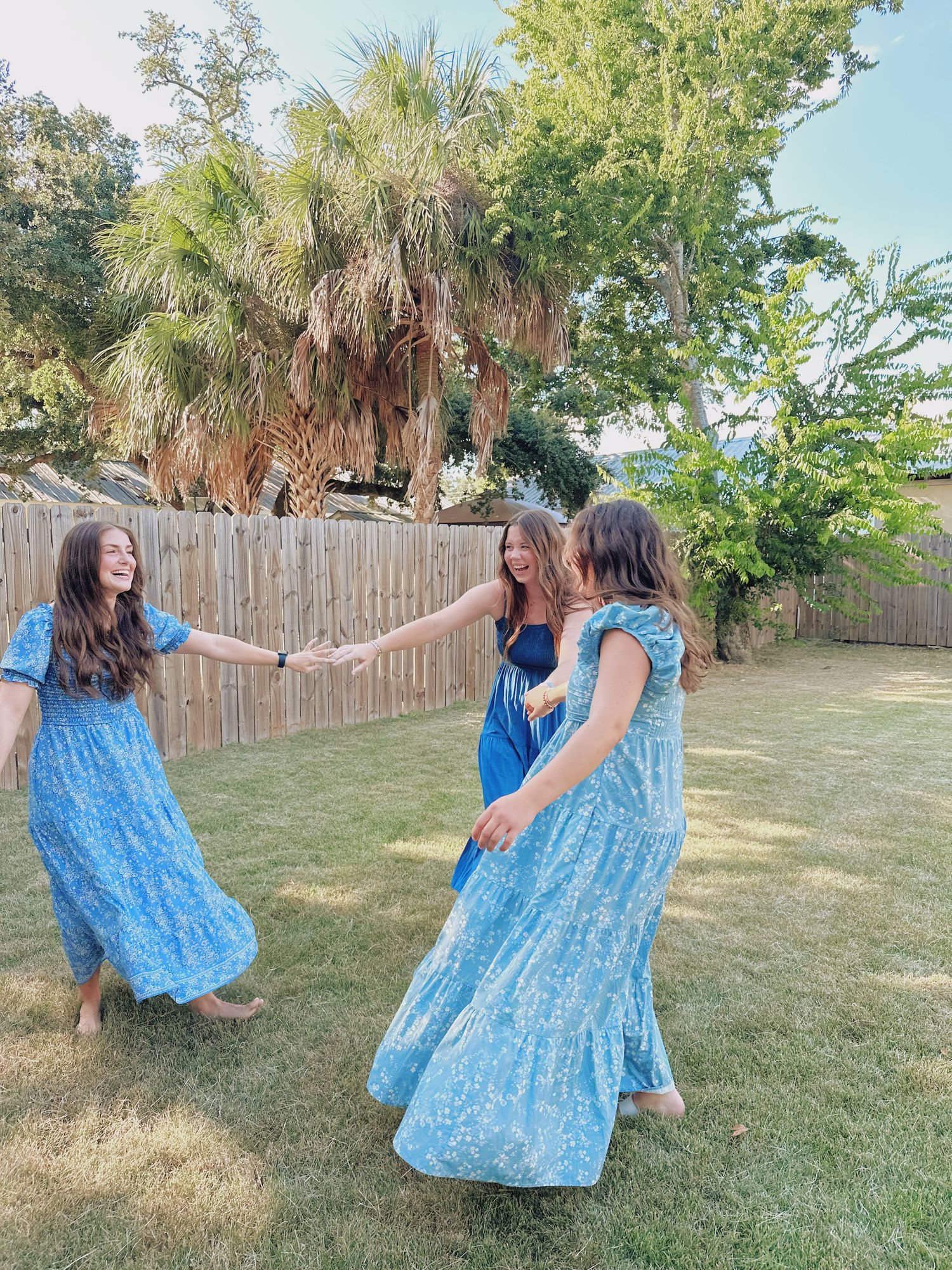 Friends in matching blue dresses twirling and dancing together in a backyard.