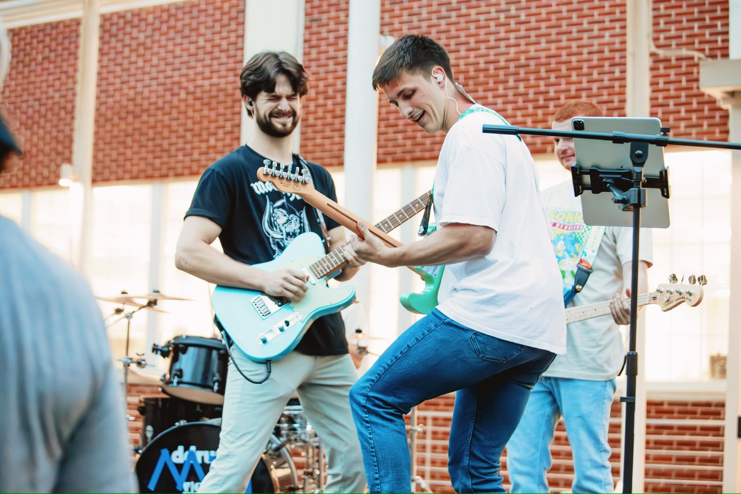 Two musicians performing energetically with electric guitars on an outdoor stage.
