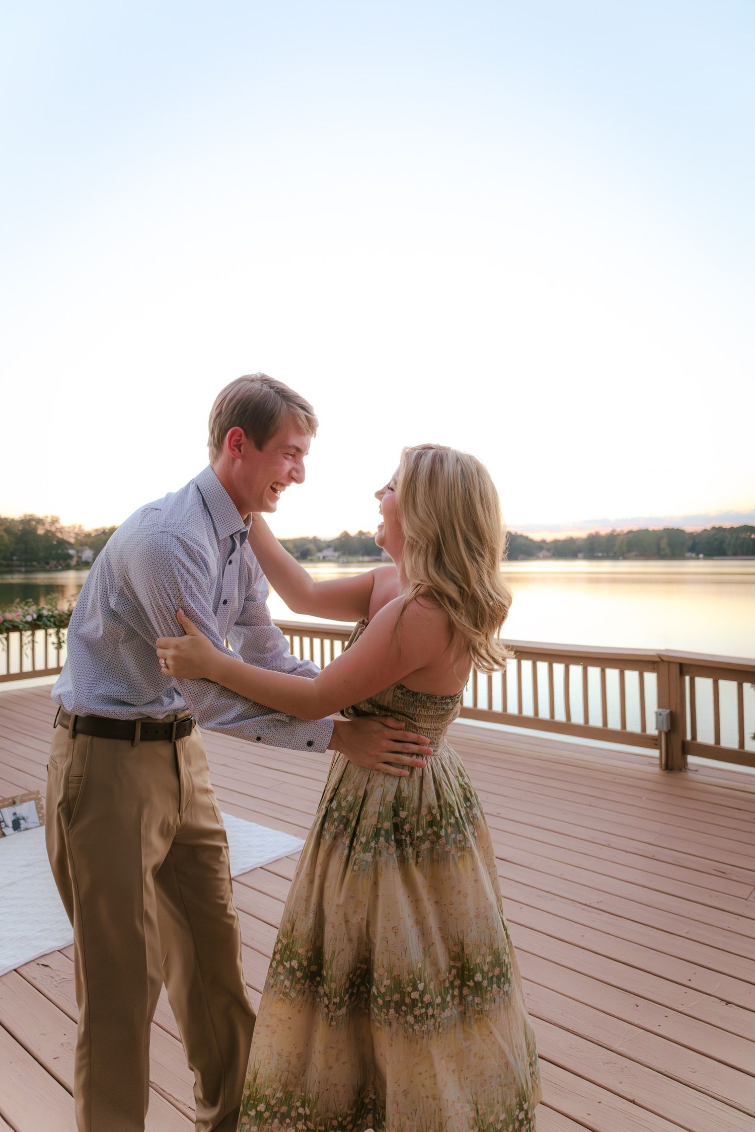 A couple dances playfully on a lakeside deck during golden hour.