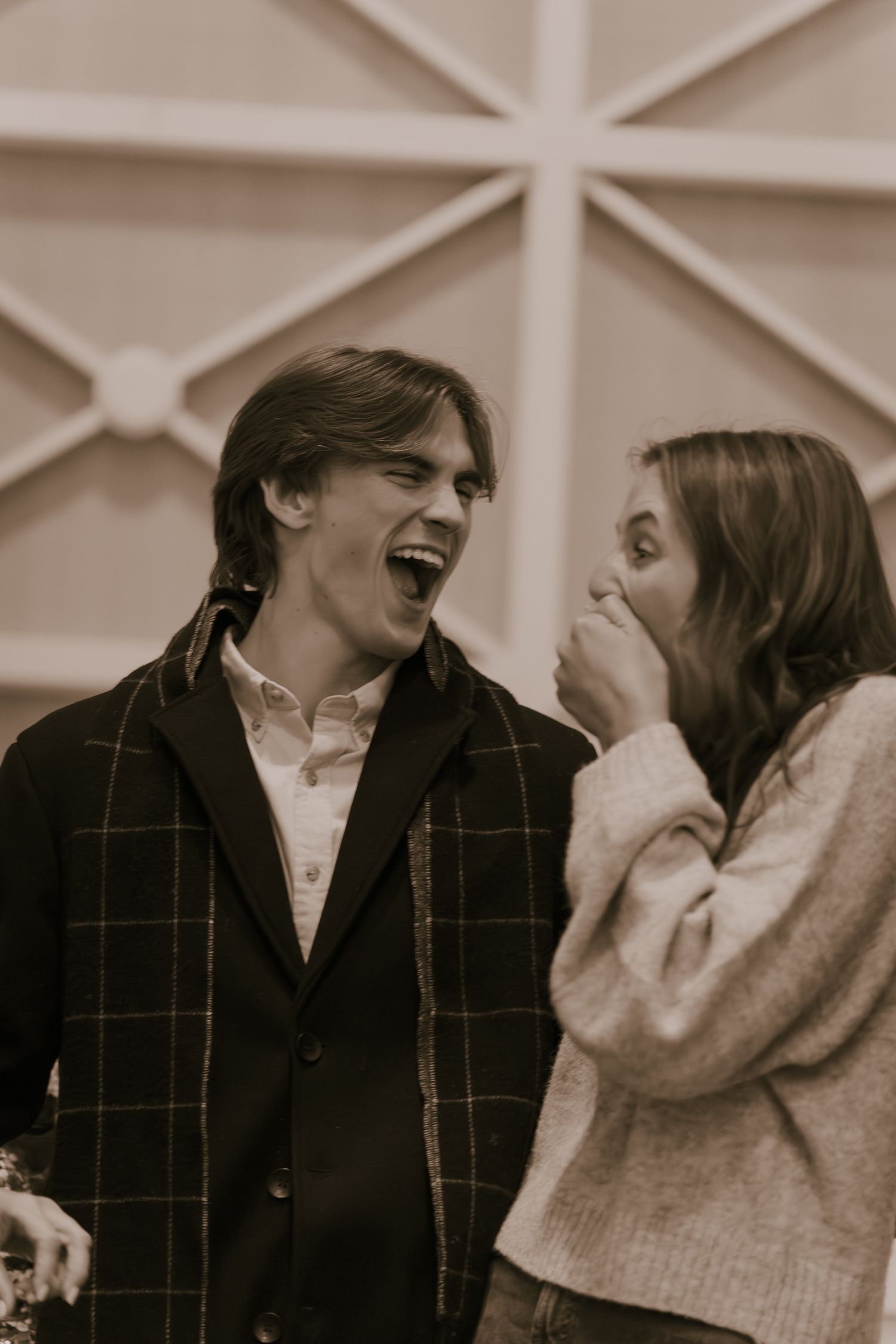 Couple laughing together indoors with geometric ceiling patterns in the background.