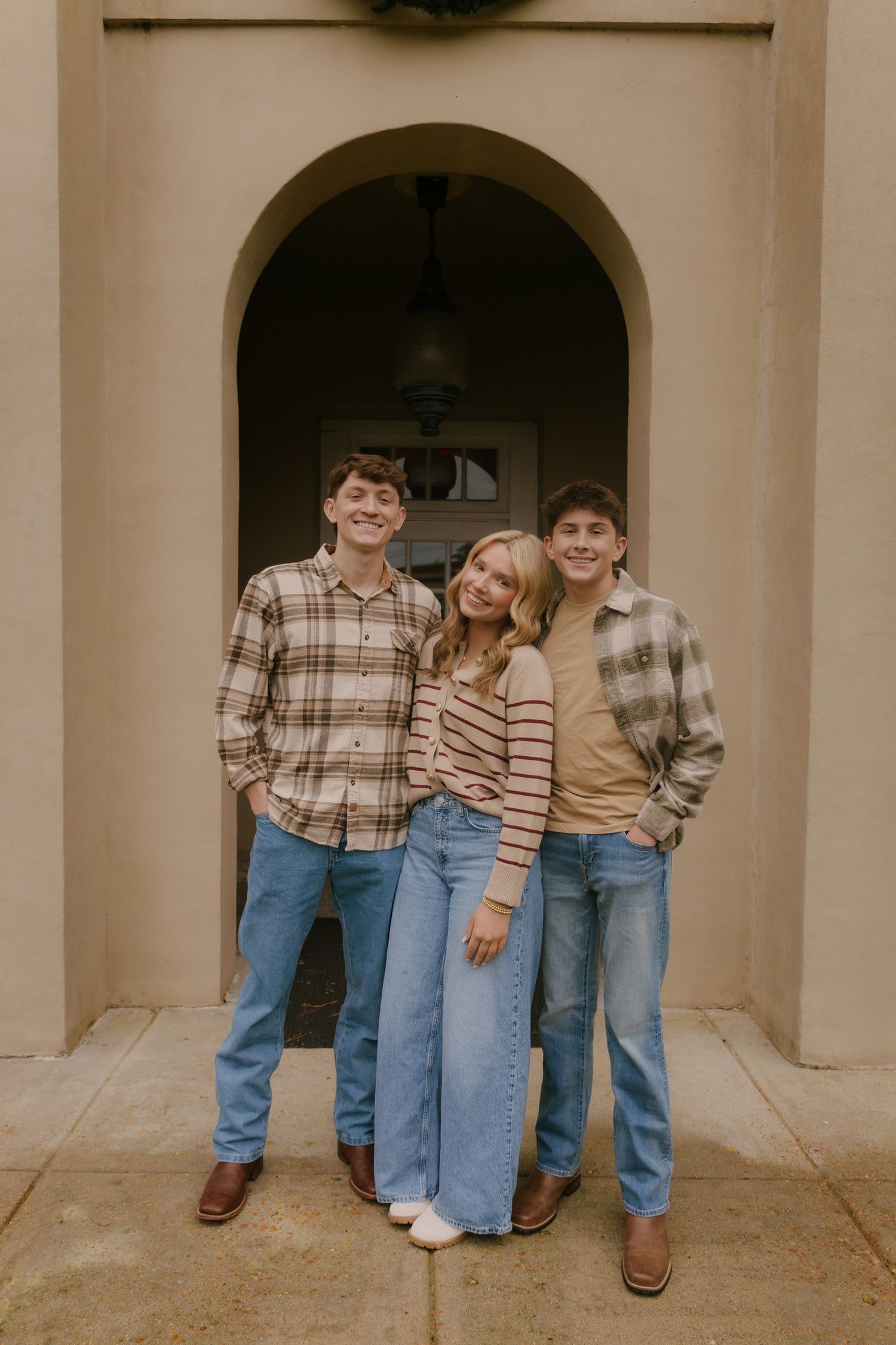 A group poses casually in front of a beige building with arched doorways.