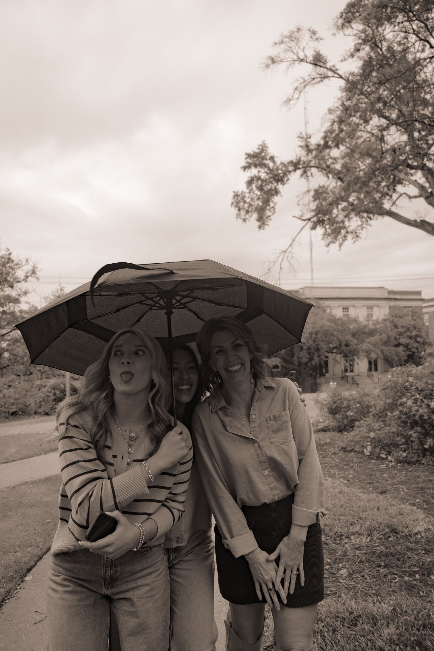 Friends share joyful moments under a black umbrella in black and white photography.