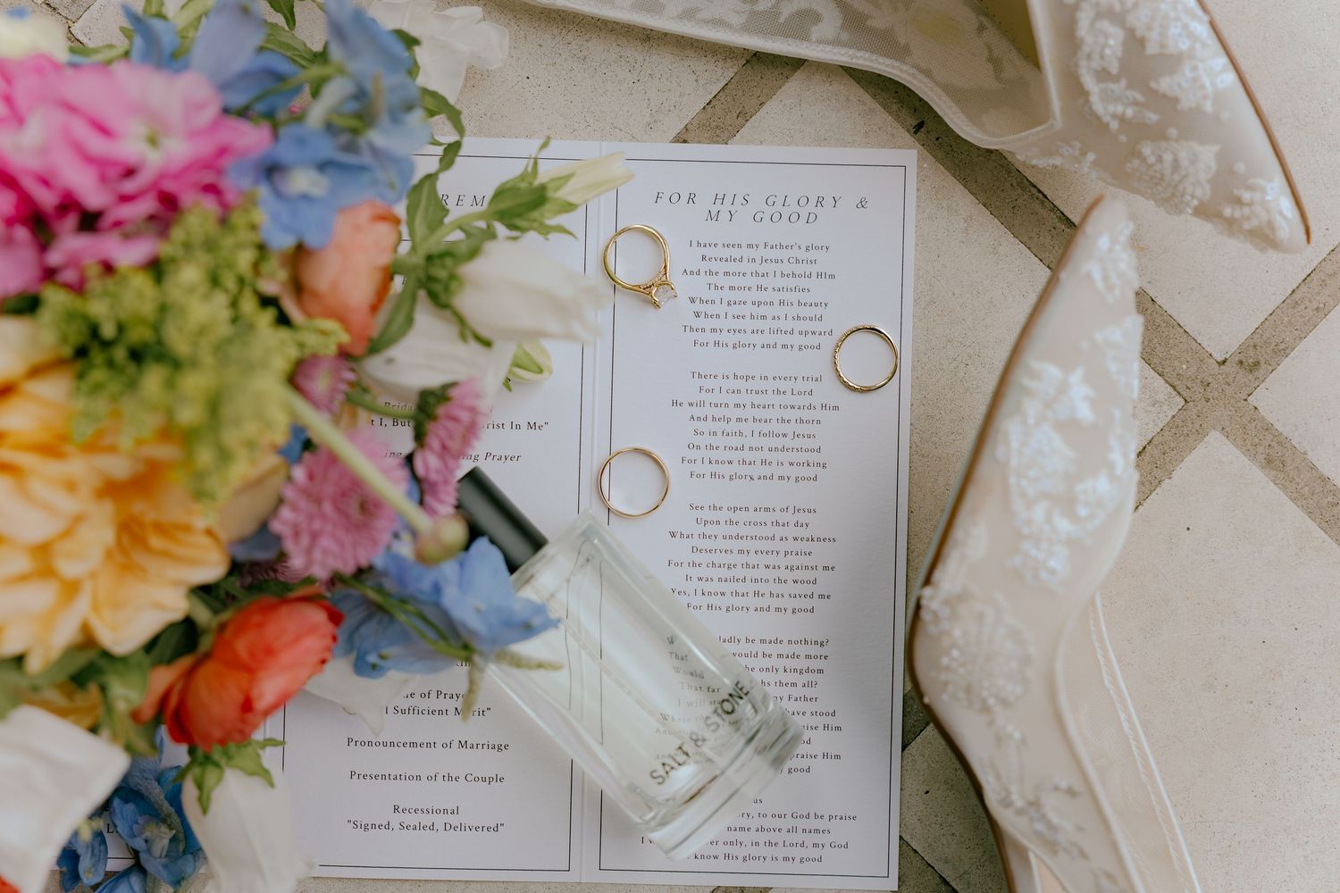 Wedding rings rest on an open book surrounded by colorful floral arrangements and delicate petals.