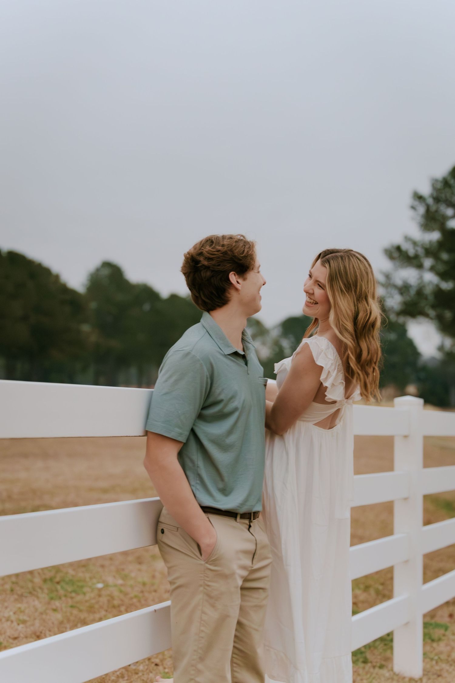 Couple sharing tender moments along a white fence in casual attire.