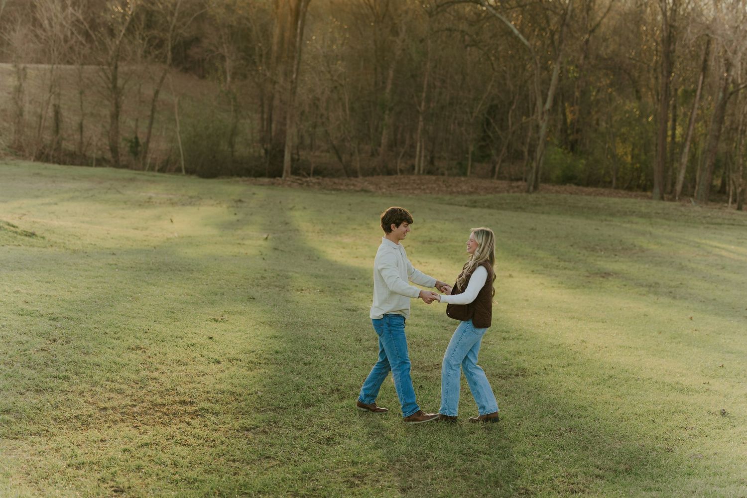 Couple walking and posing together in a scenic grassy field at sunset.