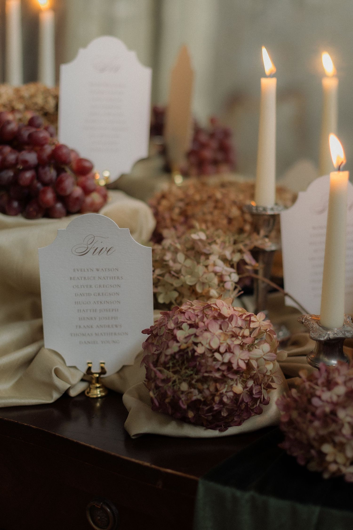 Elegant wedding table setting with white candles, dried hydrangeas, and menu cards in a romantic evening ambiance.