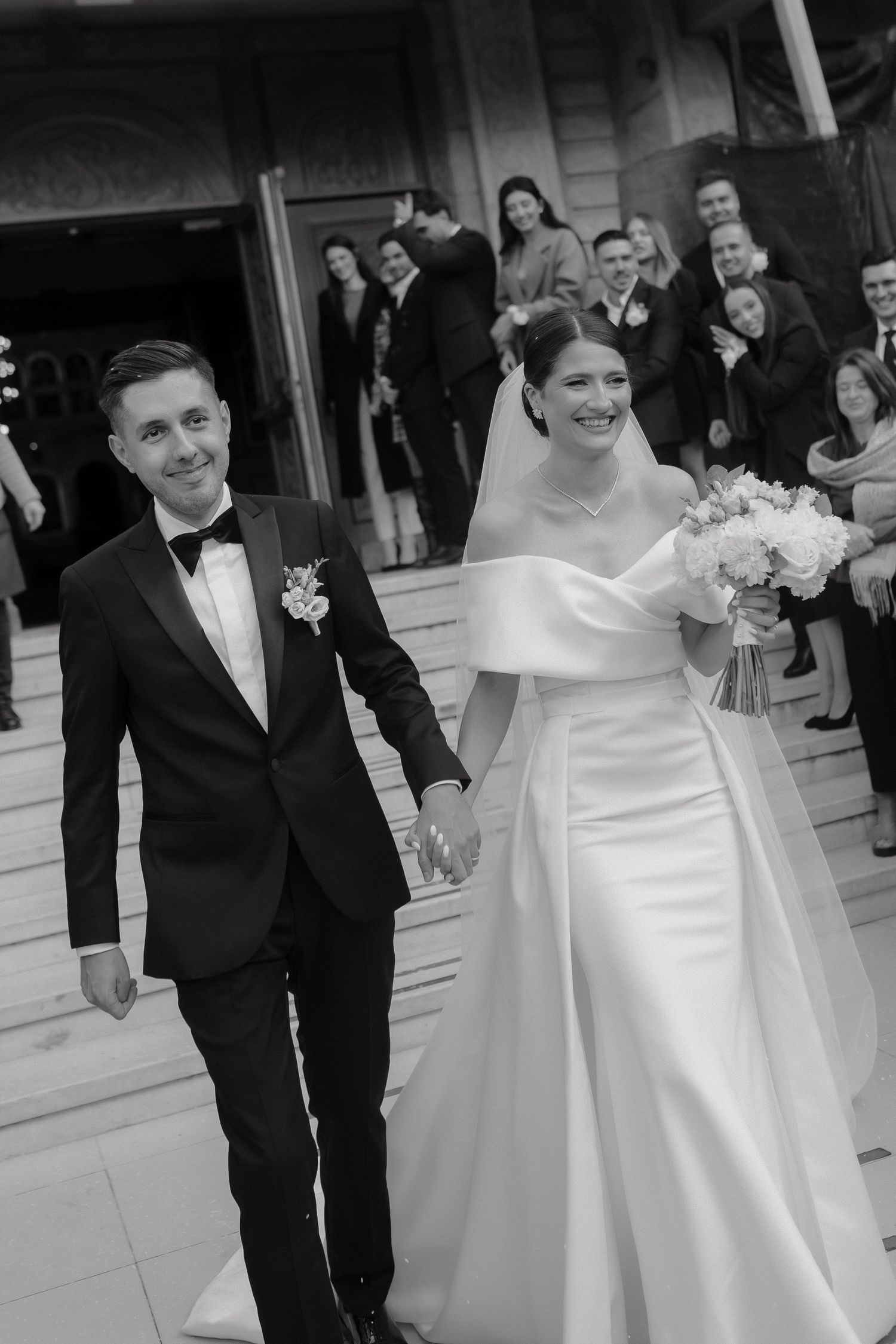 A bride and groom share a joyful moment in their wedding attire, with the bride wearing an elegant off-shoulder white gown.