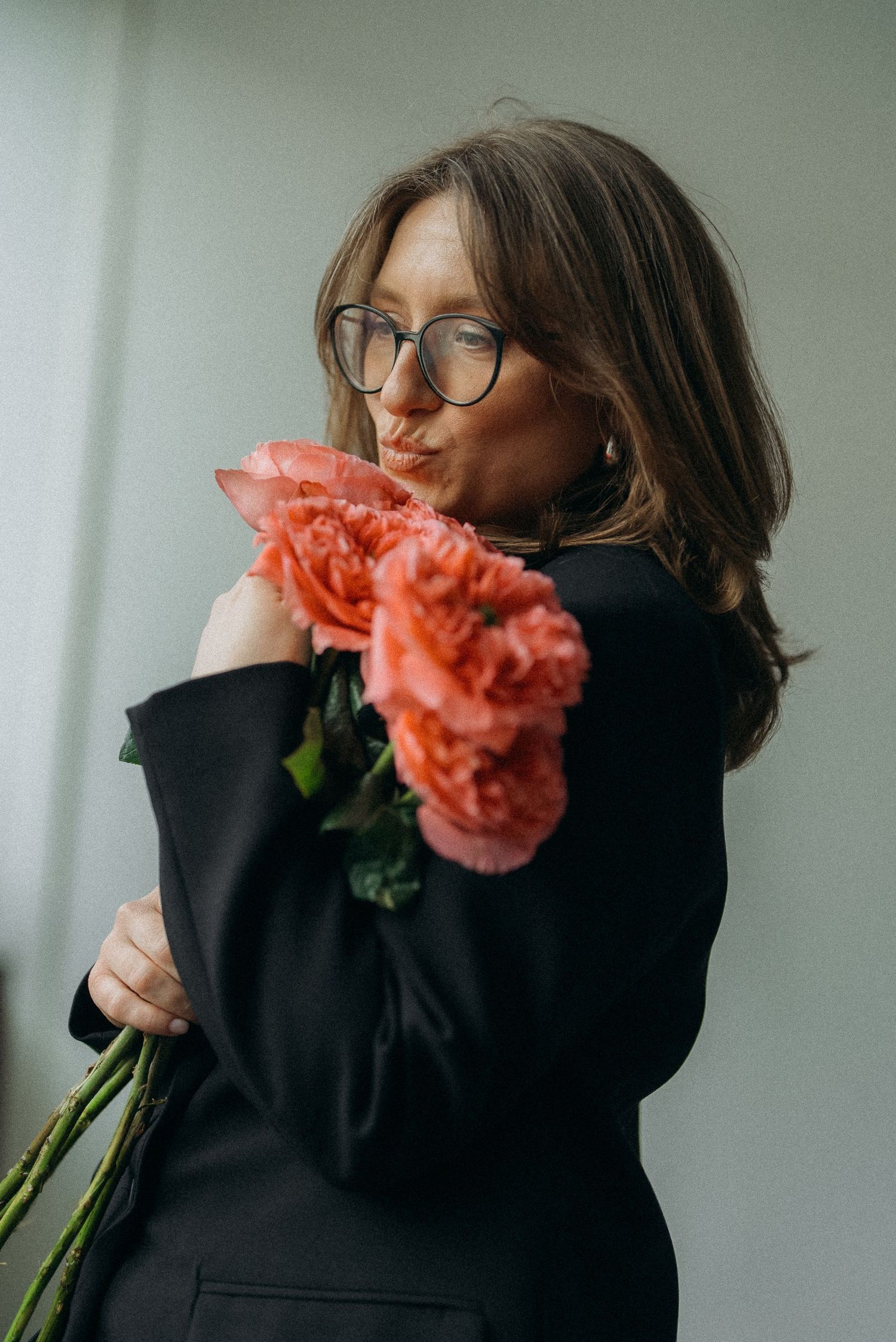 Person in black turtleneck holding vibrant coral-colored carnations against a gray background in a photo series.