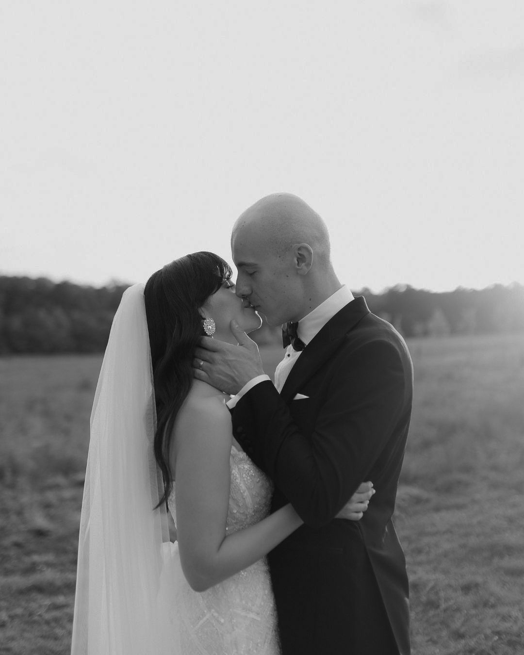 Black and white photo series of a romantic wedding couple kissing in an outdoor field at sunset.